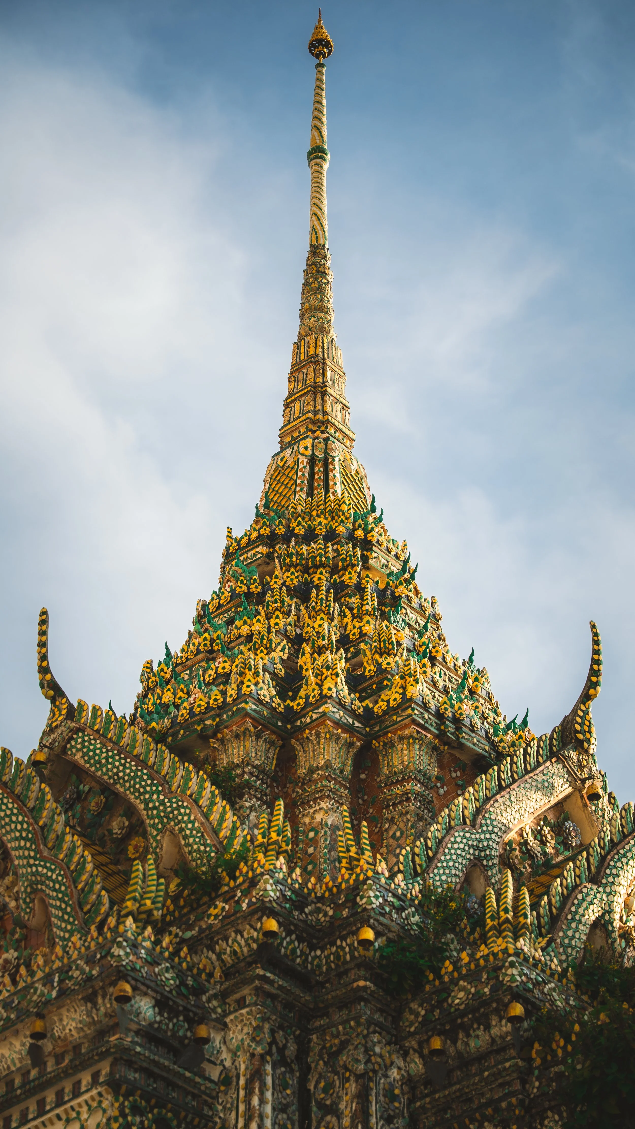 Gedetailleerde foto van een kleurrijke tempel met een hoge, smalle spits, versierd met groene, gele en gouden patronen en ornamenten, onder een blauwe lucht.
