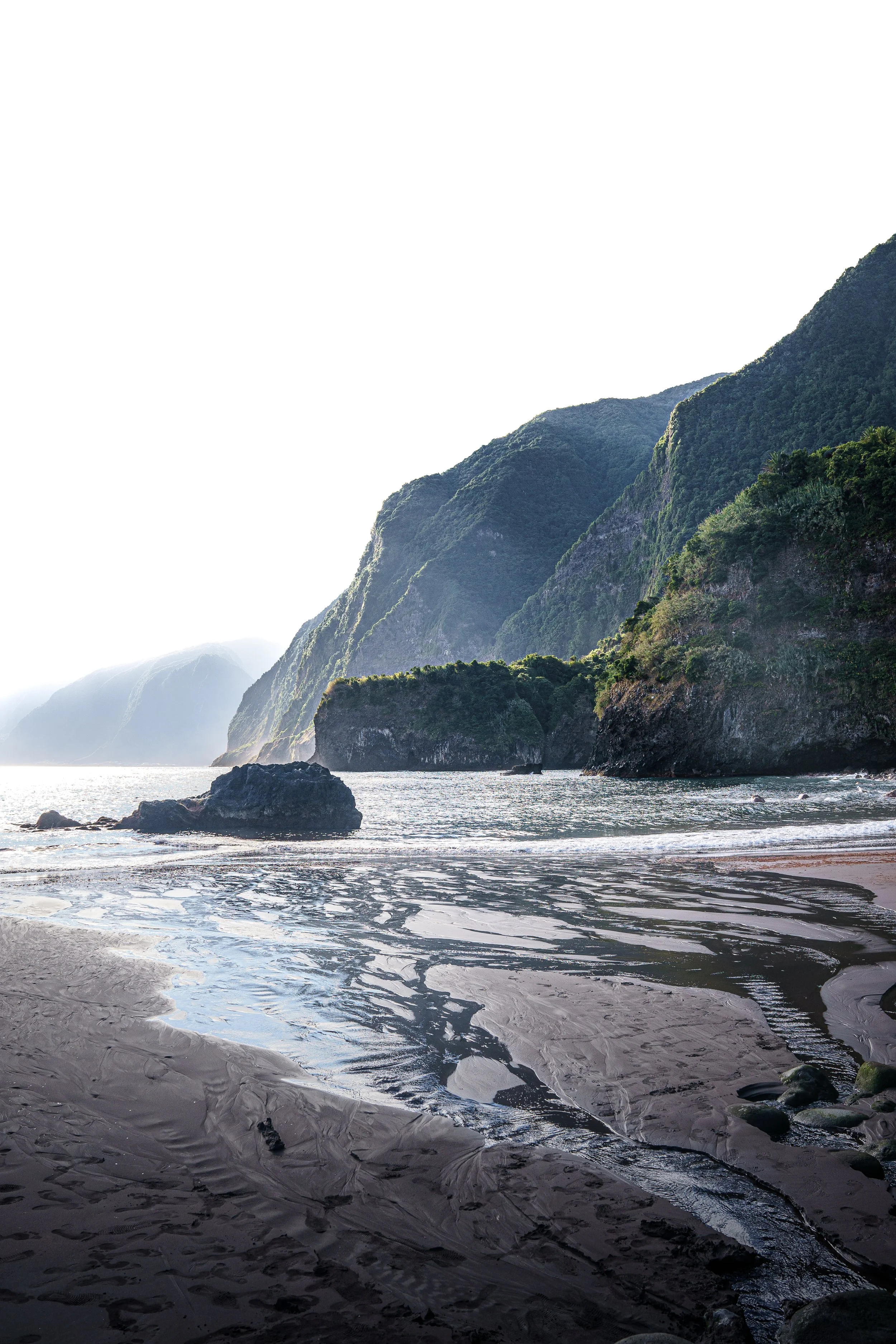 Kustlijn met rotsen en groene heuvels onder een heldere lucht.