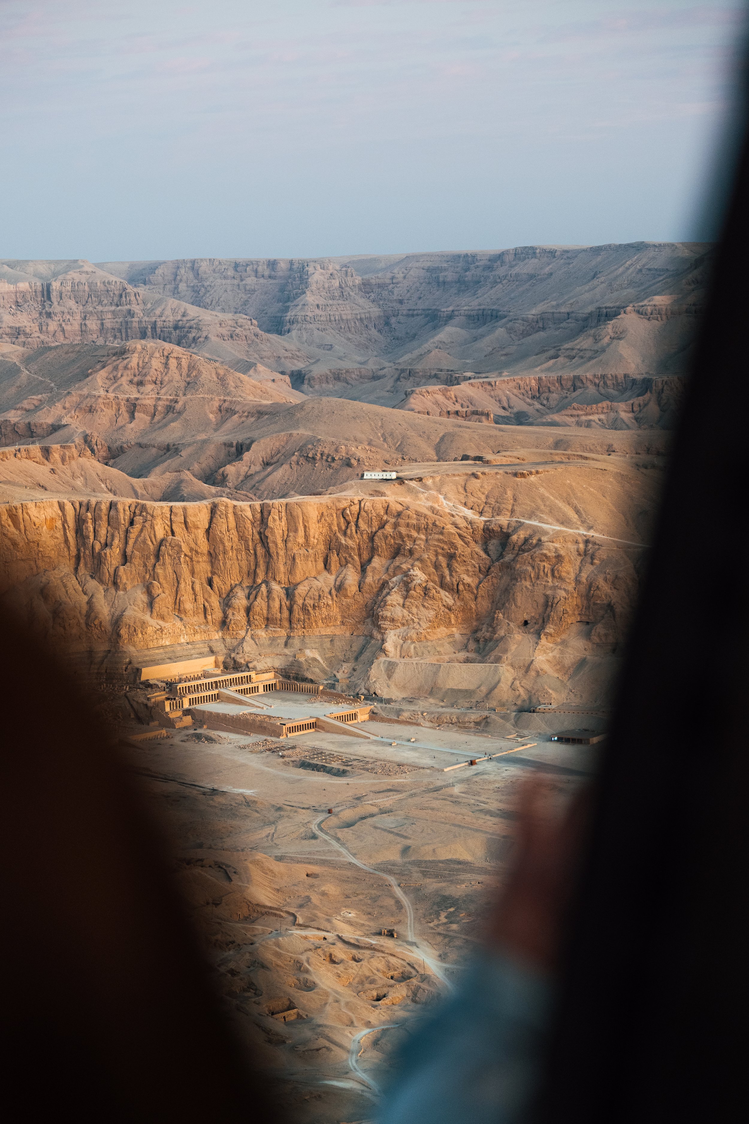 Uitzicht over de Grand Canyon met een gebouw beneden en een auto op een weg, omgeven door rotslandschap en bergen.
