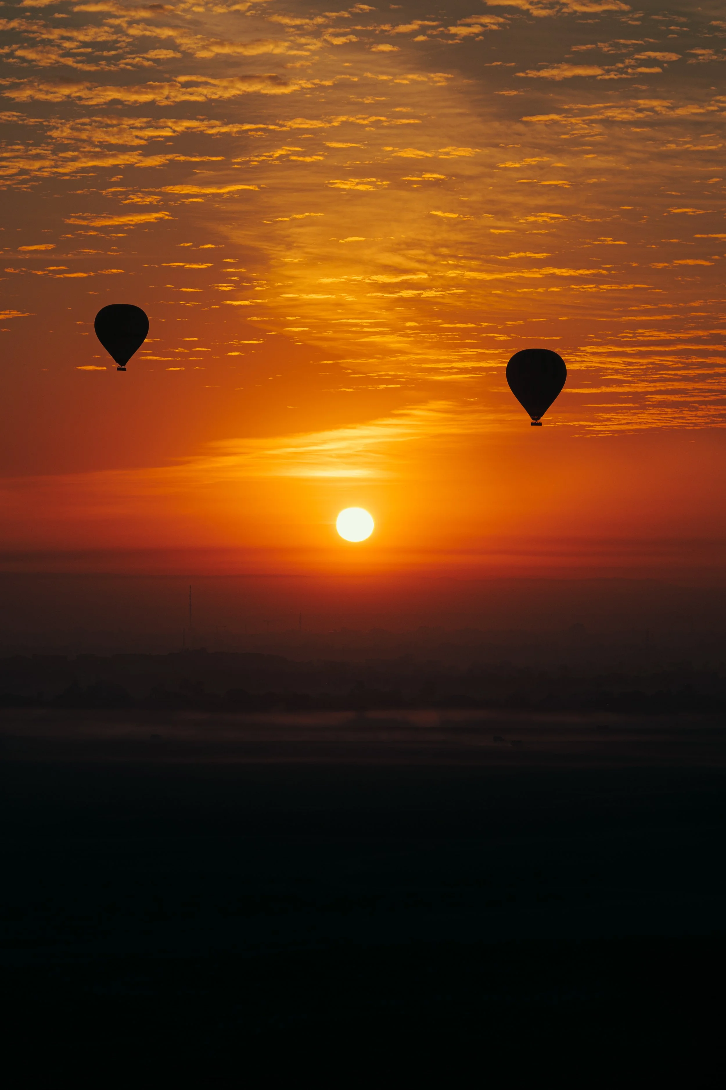 De afbeelding toont een zonsondergang met een oranje hemel en twee silhouettes van luchtballonnen in de lucht.