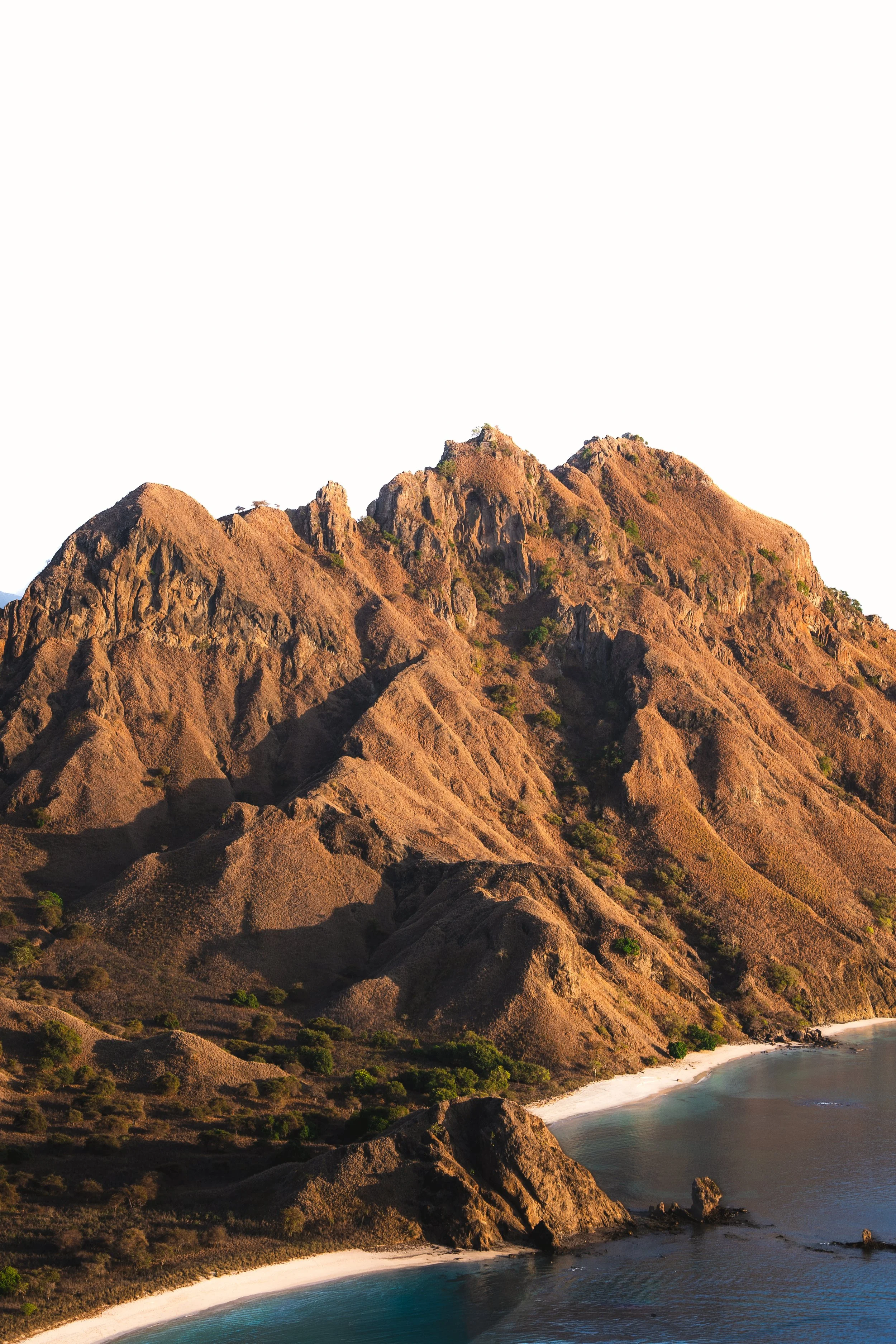 Een bergachtig landschap met droge, rotsige heuvels en een klein strand met turquoise water.