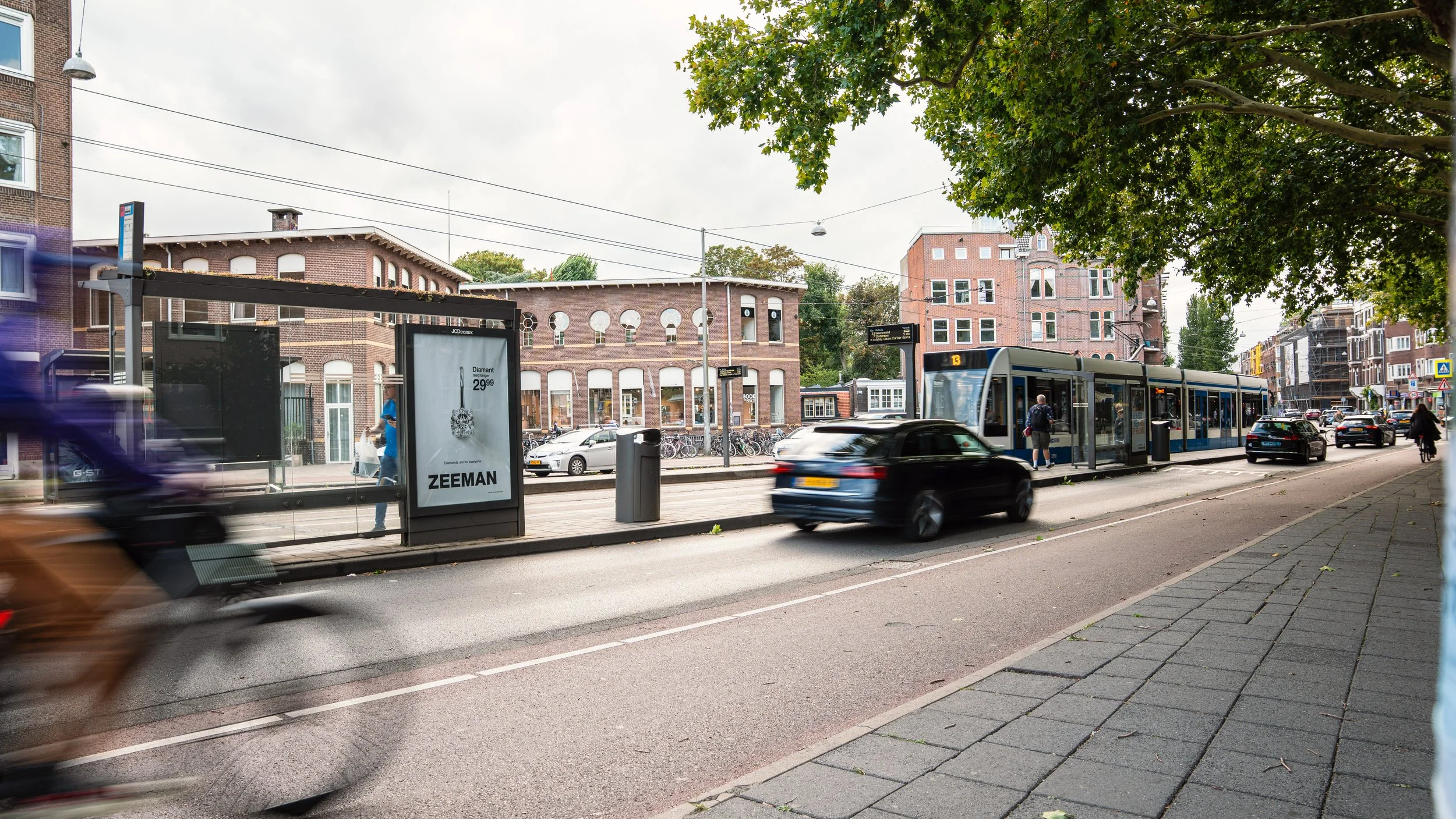 Straten in Nederland met een bushalte, een tramstation en auto's en fietsen, onder een overkapping en onder een boom, met oudere en moderne gebouwen op de achtergrond