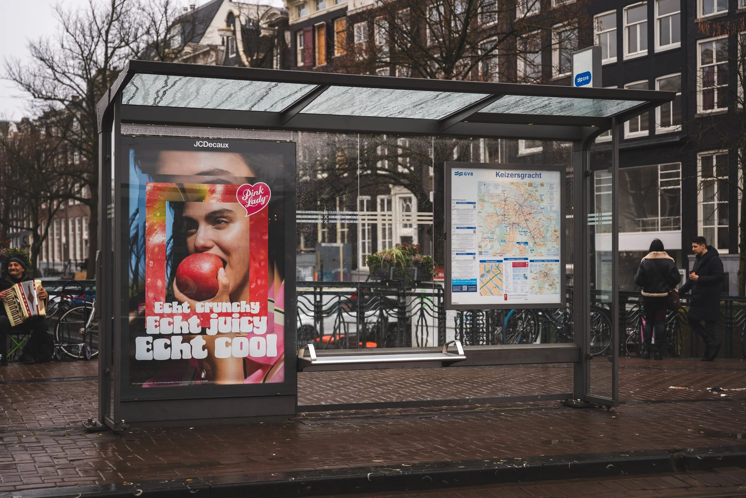 Een bushokje met een advertentie van een vrouw die op een appel bijt en een metrolijnkaart van Keizersgracht in Amsterdam, op een regenachtige dag.