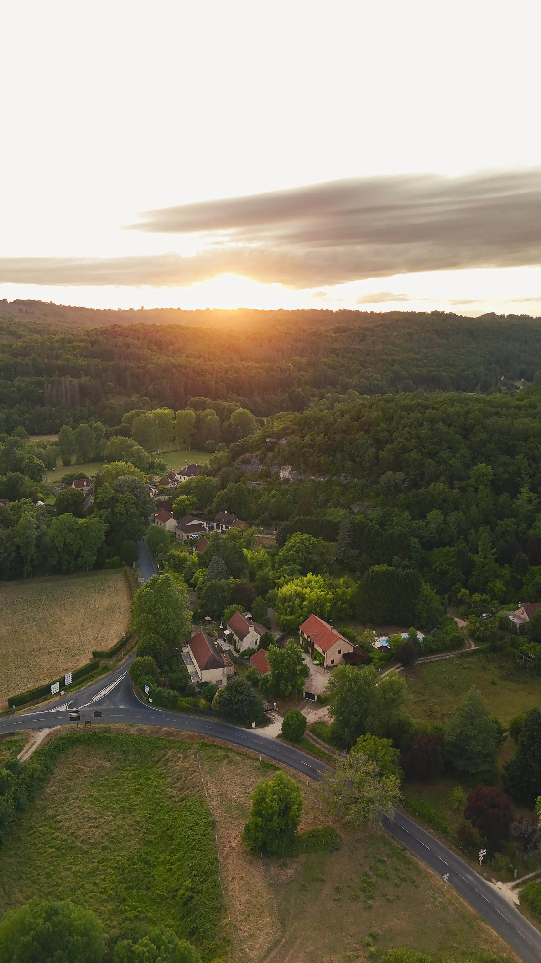 Een overzicht van een landelijk dorp met huisjes, wegen, bomen en weilanden bij zonsondergang.