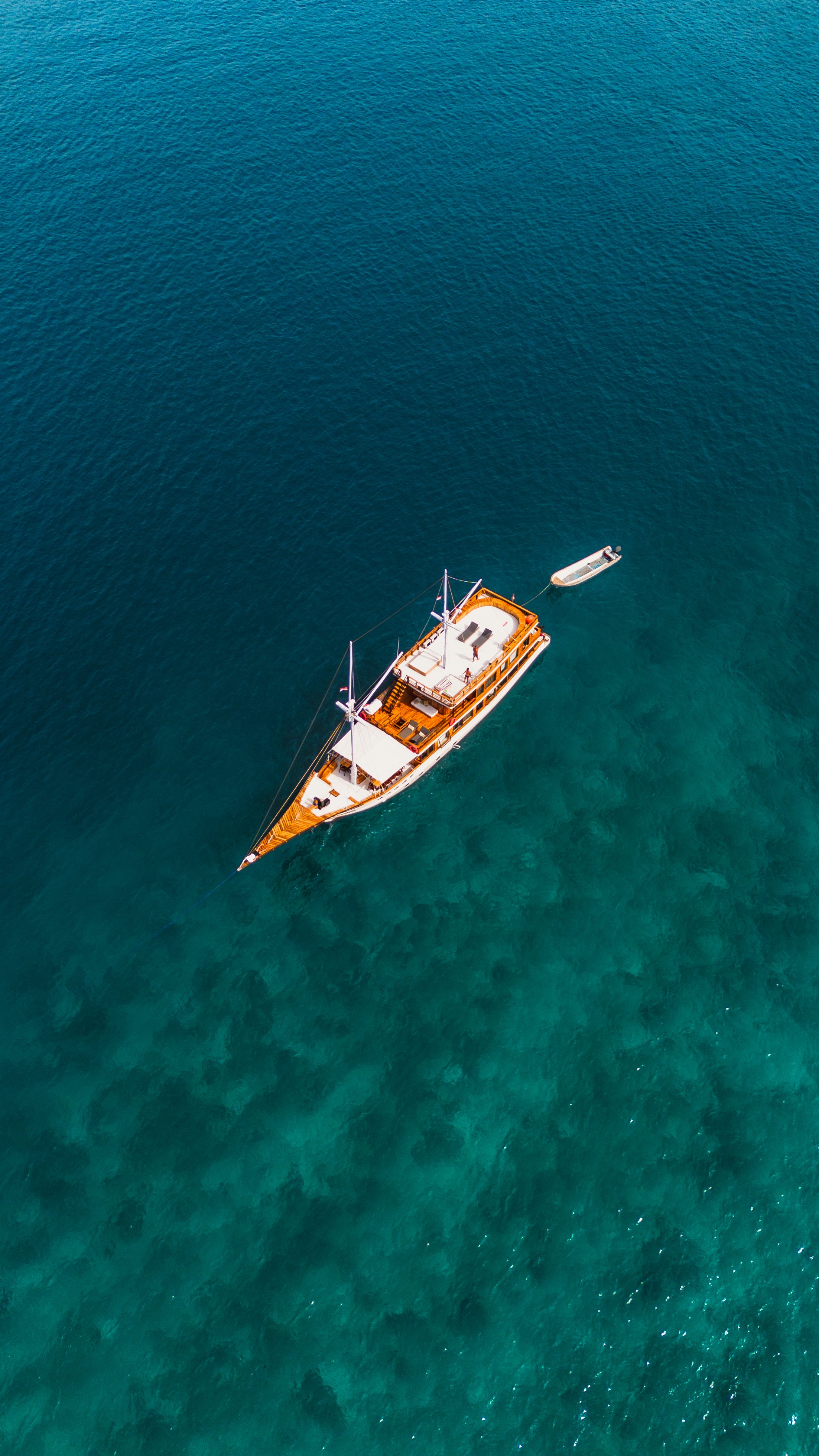 Een motorjacht en een kleinere boot drijven op een helderblauwe zee, gevangen vanuit een vogelperspectief.
