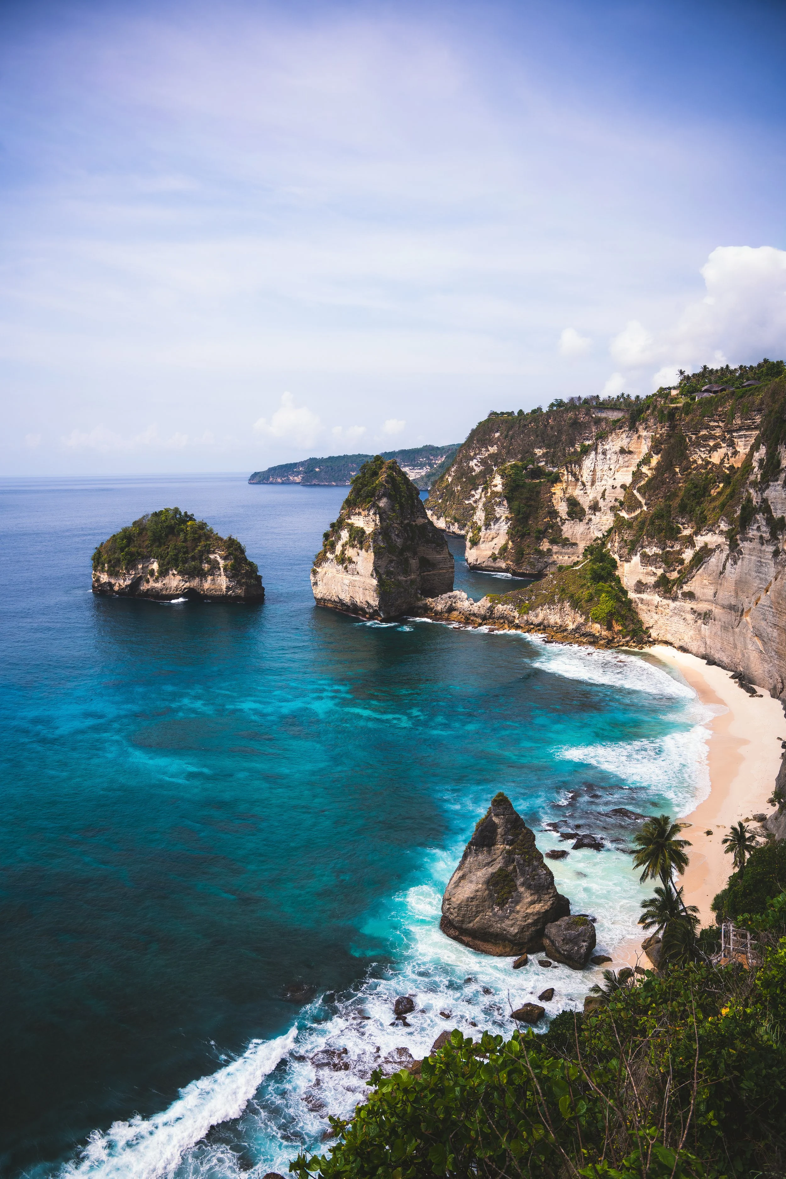 Kustlijn met kliffen, rotsen en een strand, omgeven door natuur en oceaan, onder een blauwe hemel.