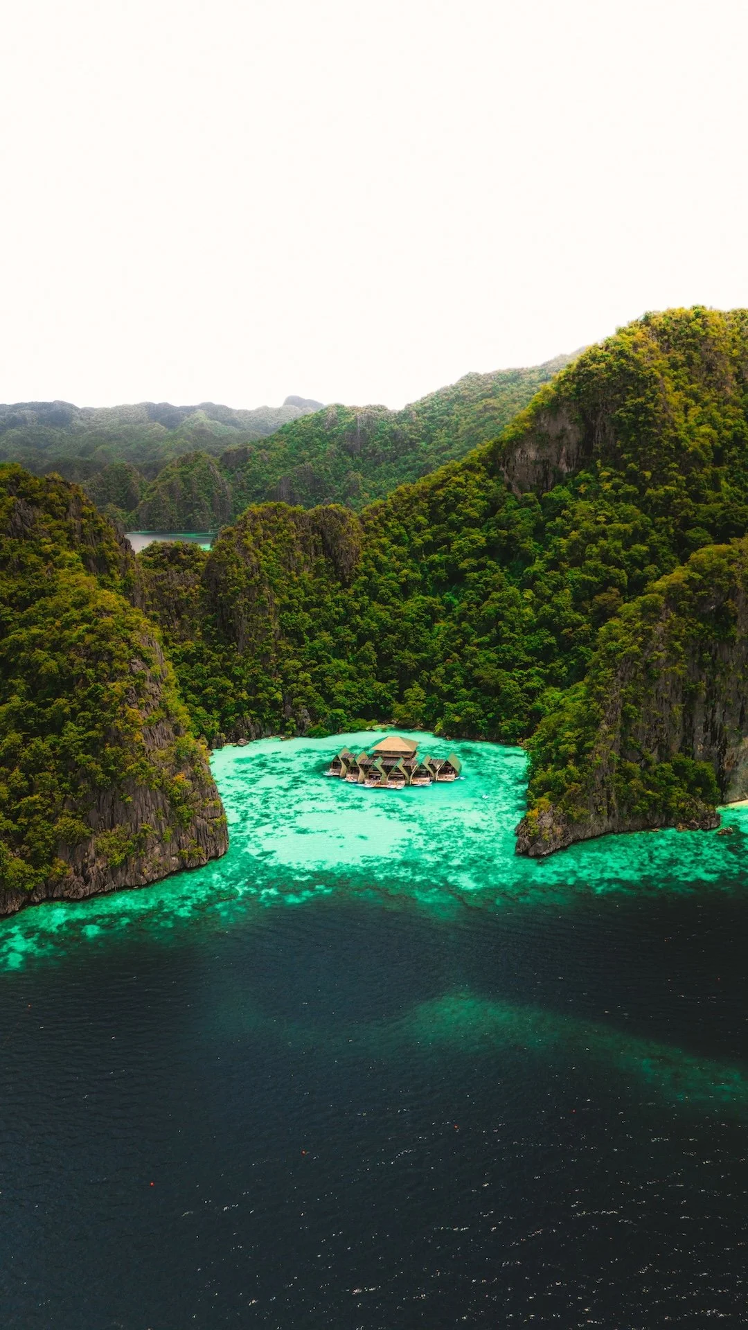 Landschap met groene heuvels, turquoise water en een rotshotel in het water.