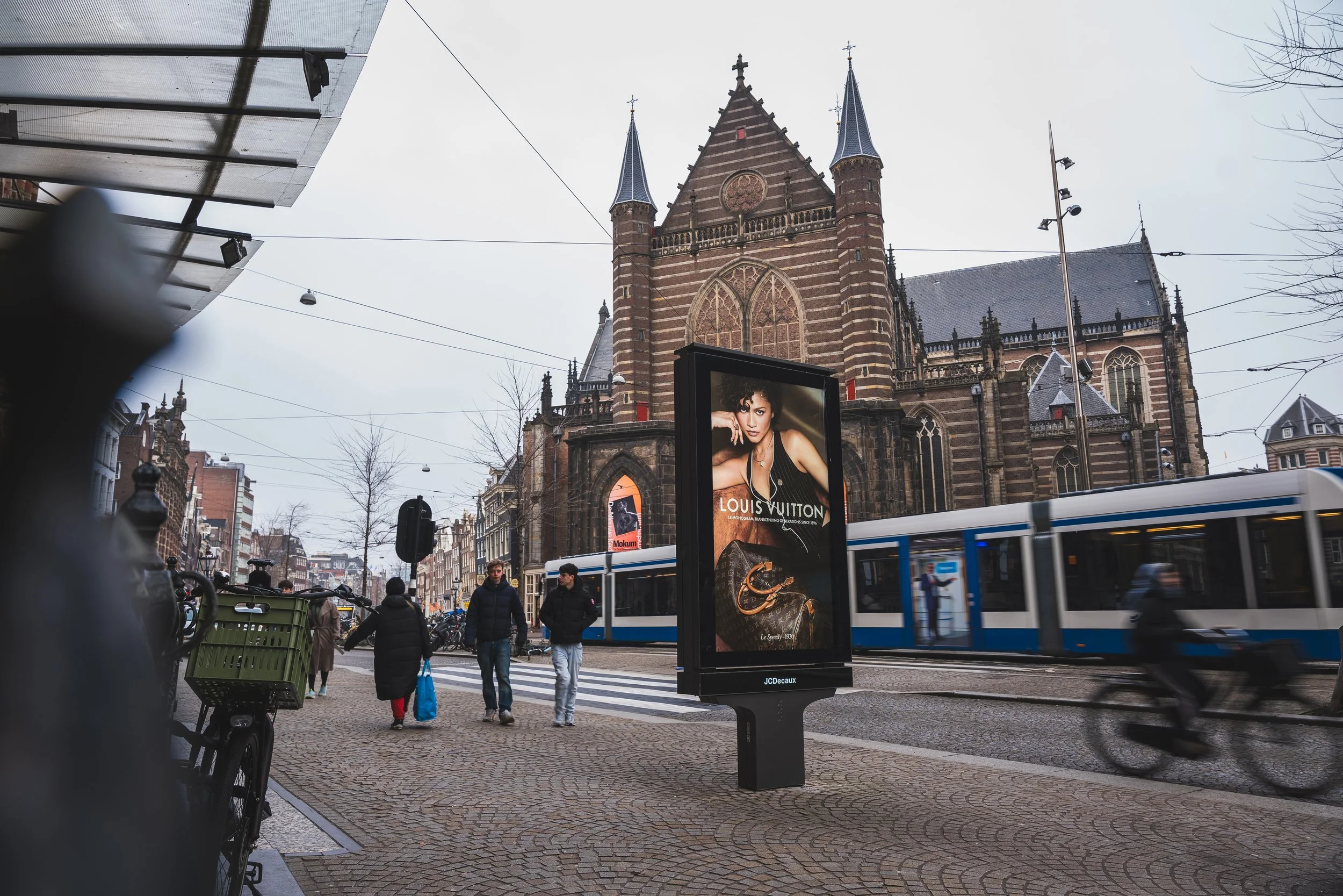 Straatbeeld met passant, tram en een advertentiebord voor Louis Vuitton voor een kerk in Nederland.