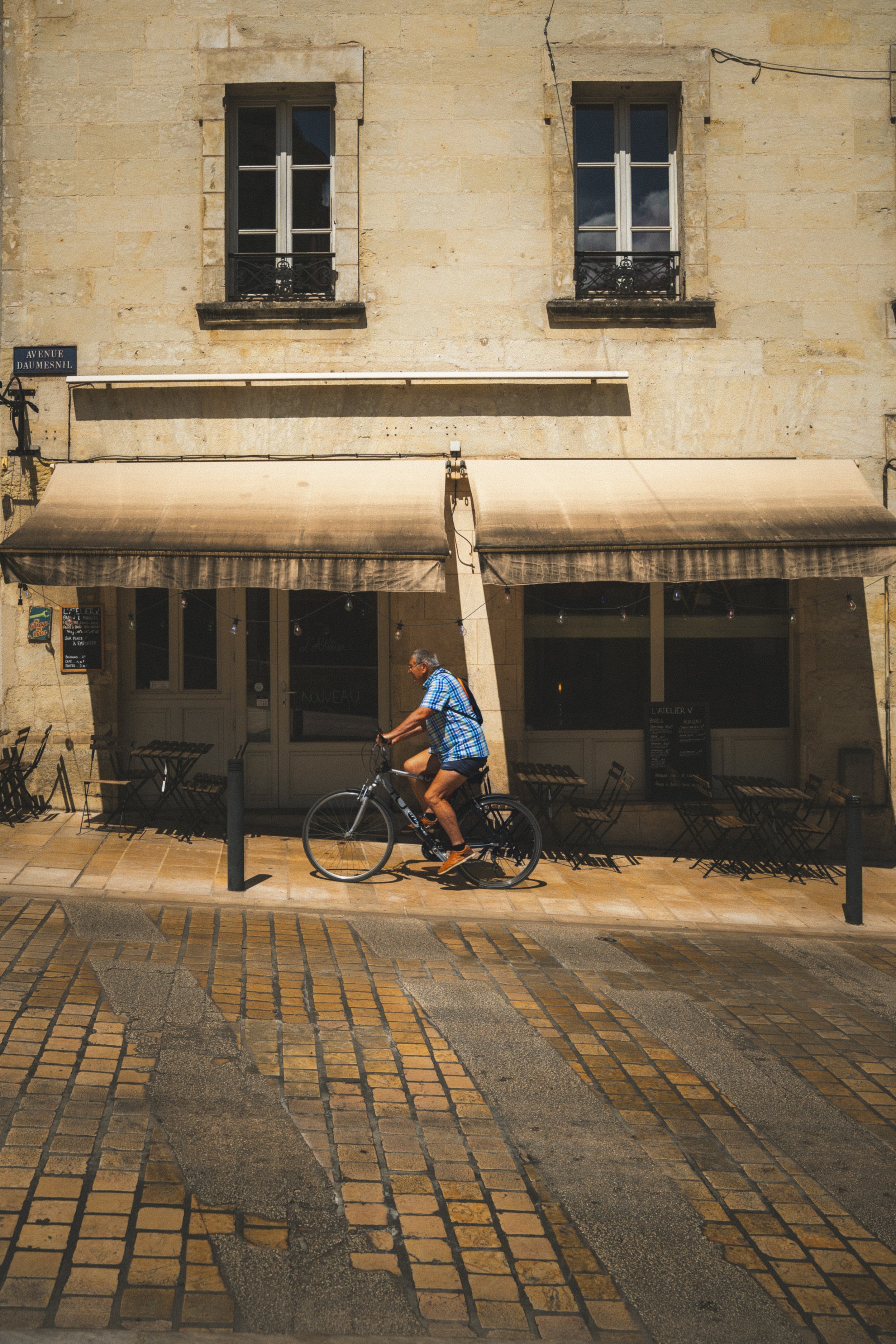 Man fietst langs een café met een gevouwen paraplu aan de gevel, op een stoffige straat met betonnen stenen.