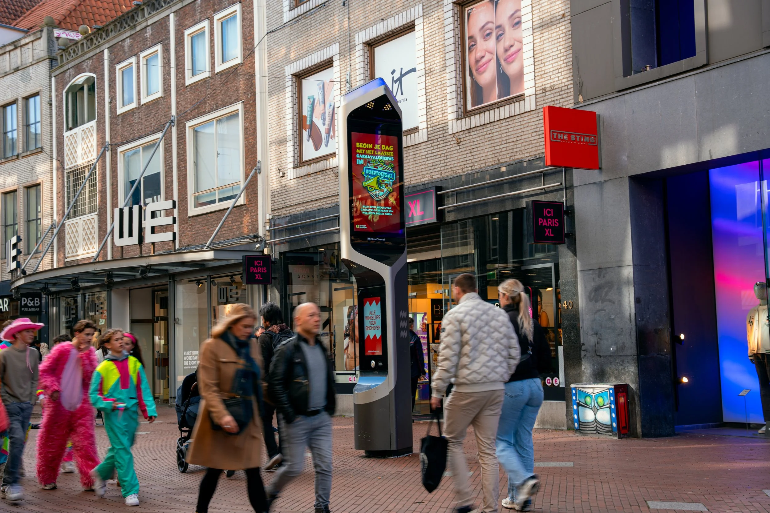 Straatbeeld met mensen die wandelen, winkels en digitale reclameborden, met een opvallendige digitale billboard en een gebouw met reclame en grote posters.