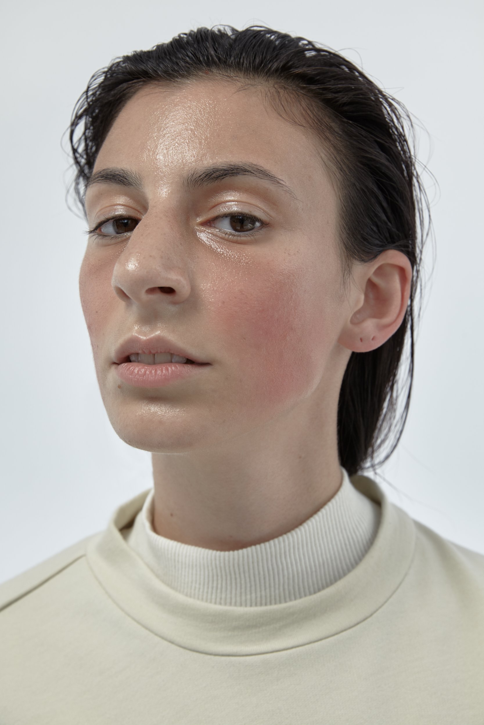 Close-up of a young woman with short dark hair, wearing a light-colored turtleneck sweater, against a plain white background.