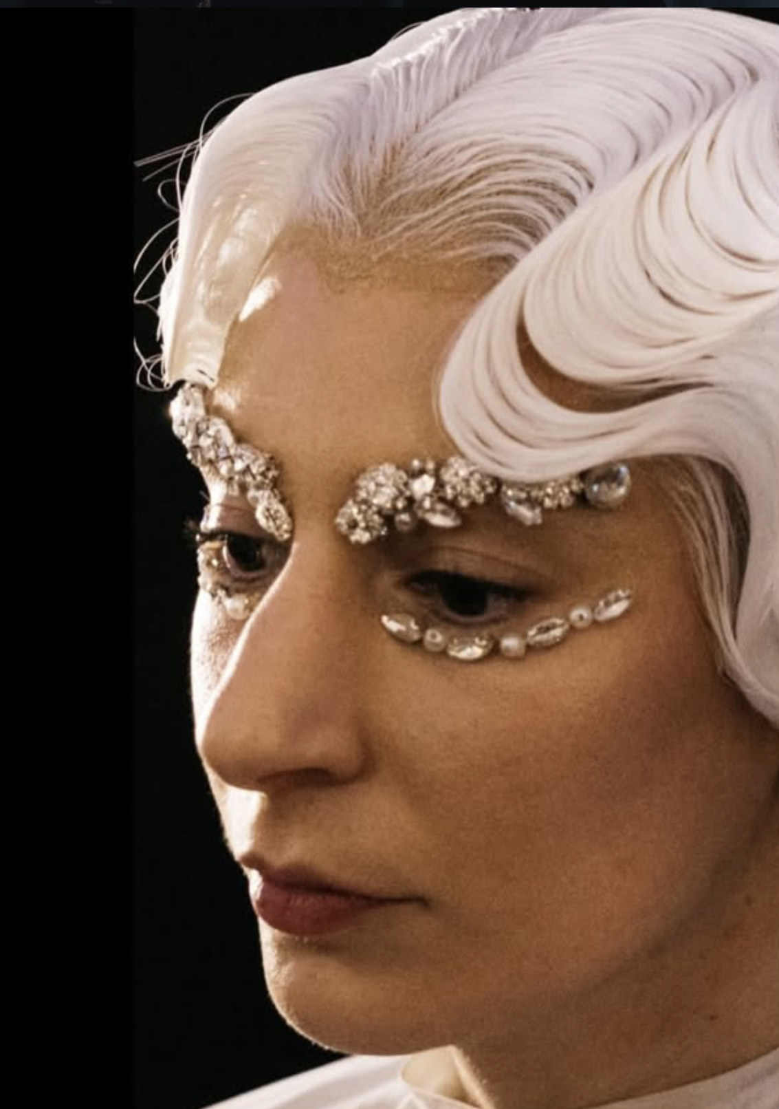 Close-up of a person with platinum blonde hair and elaborate rhinestone and pearl facial jewelry.