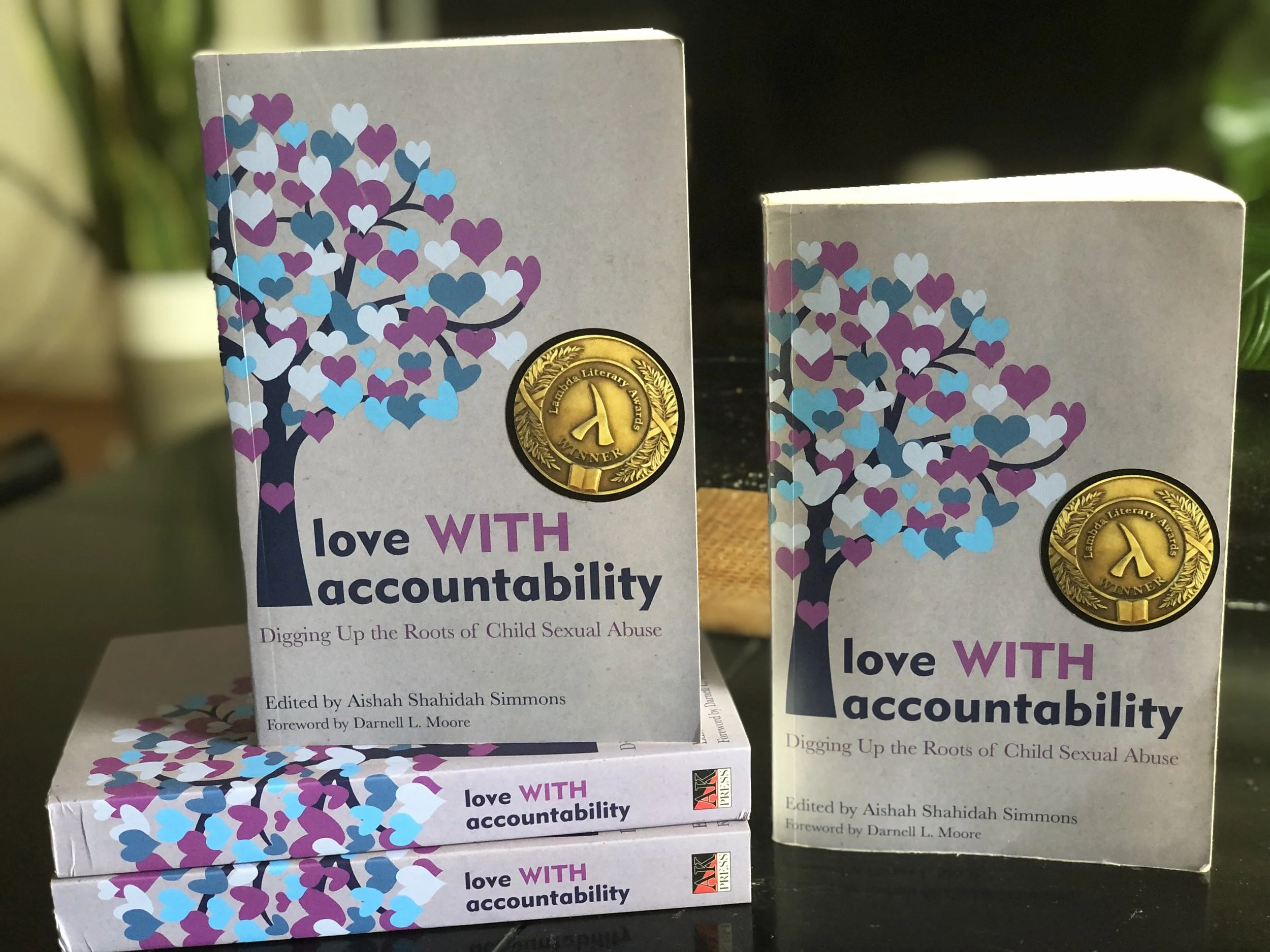Books titled "Love With Accountability" with a cover illustration of a heart-shaped tree and a gold Medal of Merit award, placed on a table.