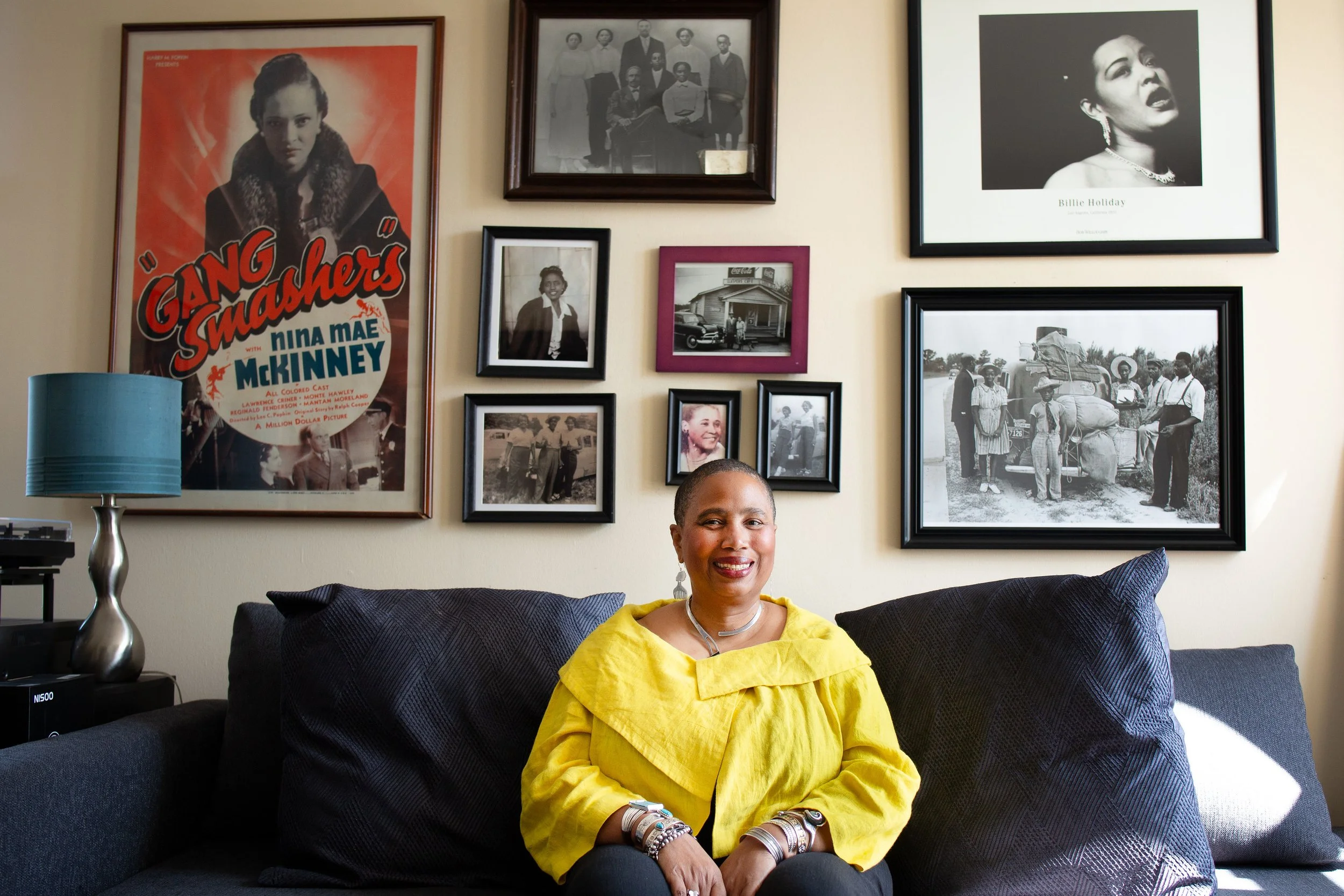 Aishah Shahidah Simmons on a sofa beneath a gallery wall of ancestor and cultural icons. Photo by Studio TSHAY.