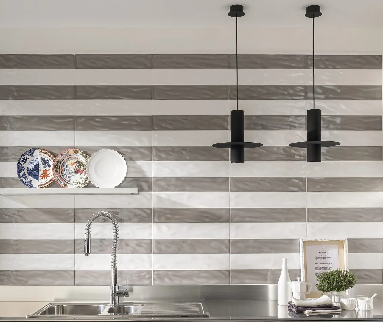 Modern kitchen with black pendant lights, a strip of decorative plates on a shelf, and a stainless steel sink.