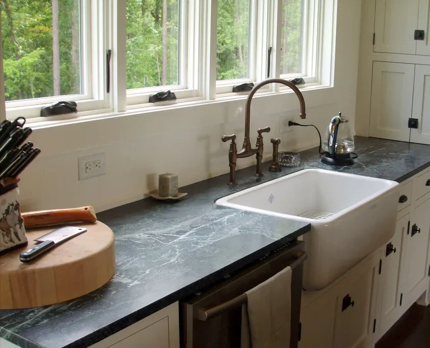 Kitchen sink with a window above, kitchen counter with a knife block, salt and pepper shaker, and a soap dispenser.