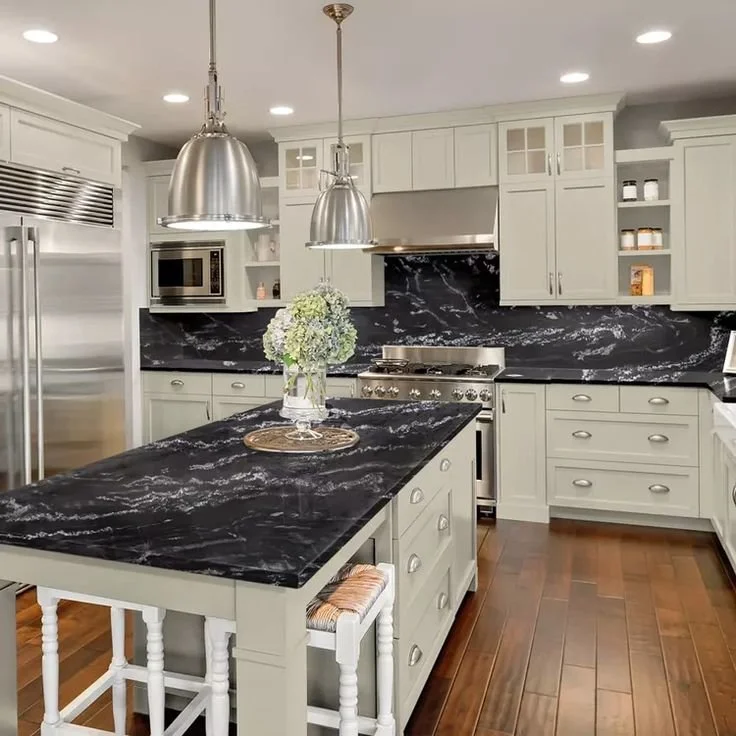 Kitchen with black marble countertops, white cabinets, stainless steel appliances including refrigerator, microwave, stove, and oven, and wooden flooring.