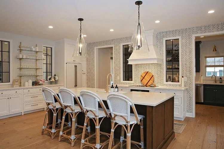 Modern kitchen with a large white island, white cabinetry, pendant lights, bar stools, and a patterned wallpaper accent wall.