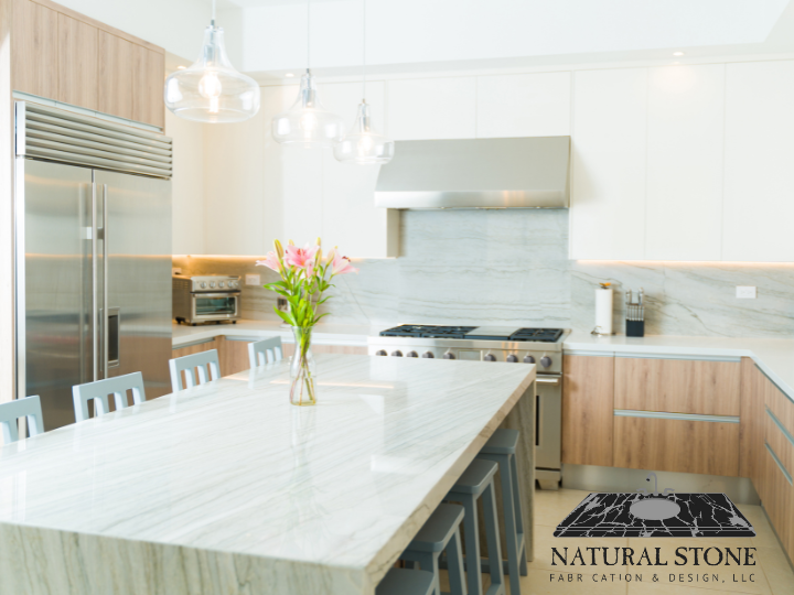Modern kitchen with a large marble island, stainless steel appliances, a bouquet of pink flowers in a glass vase, and pendant lighting.