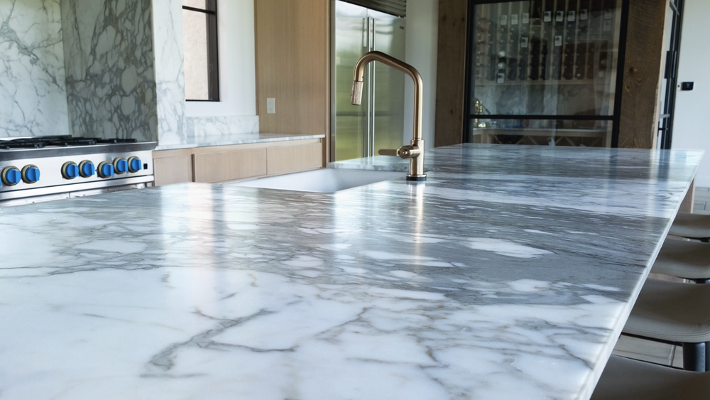 Modern kitchen with marble countertop island, brass faucet, cooktop, and wood cabinetry.