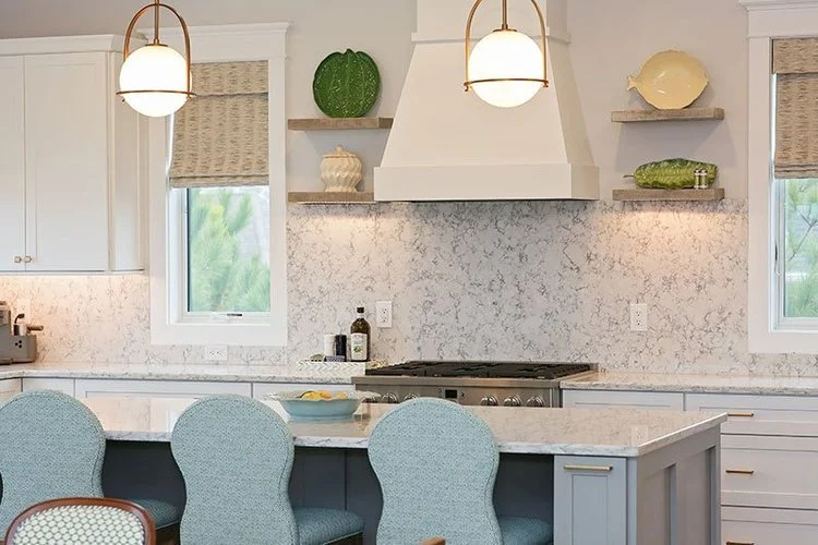 Modern kitchen with white cabinets, marble countertops, pendant lighting, and open shelving displaying decorative items and plants.