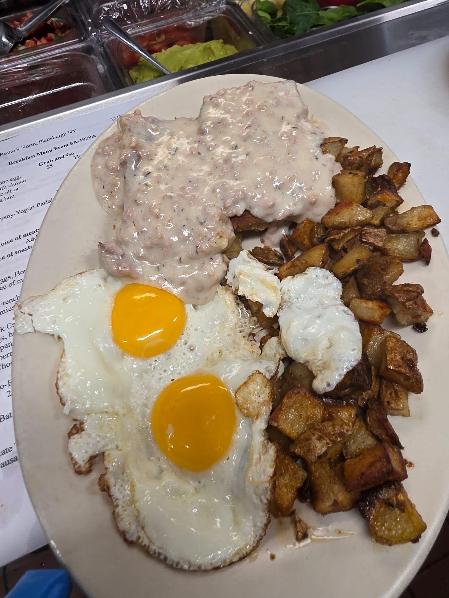 Plate with two sunny side up eggs, fried potatoes, and biscuits with sausage gravy.
