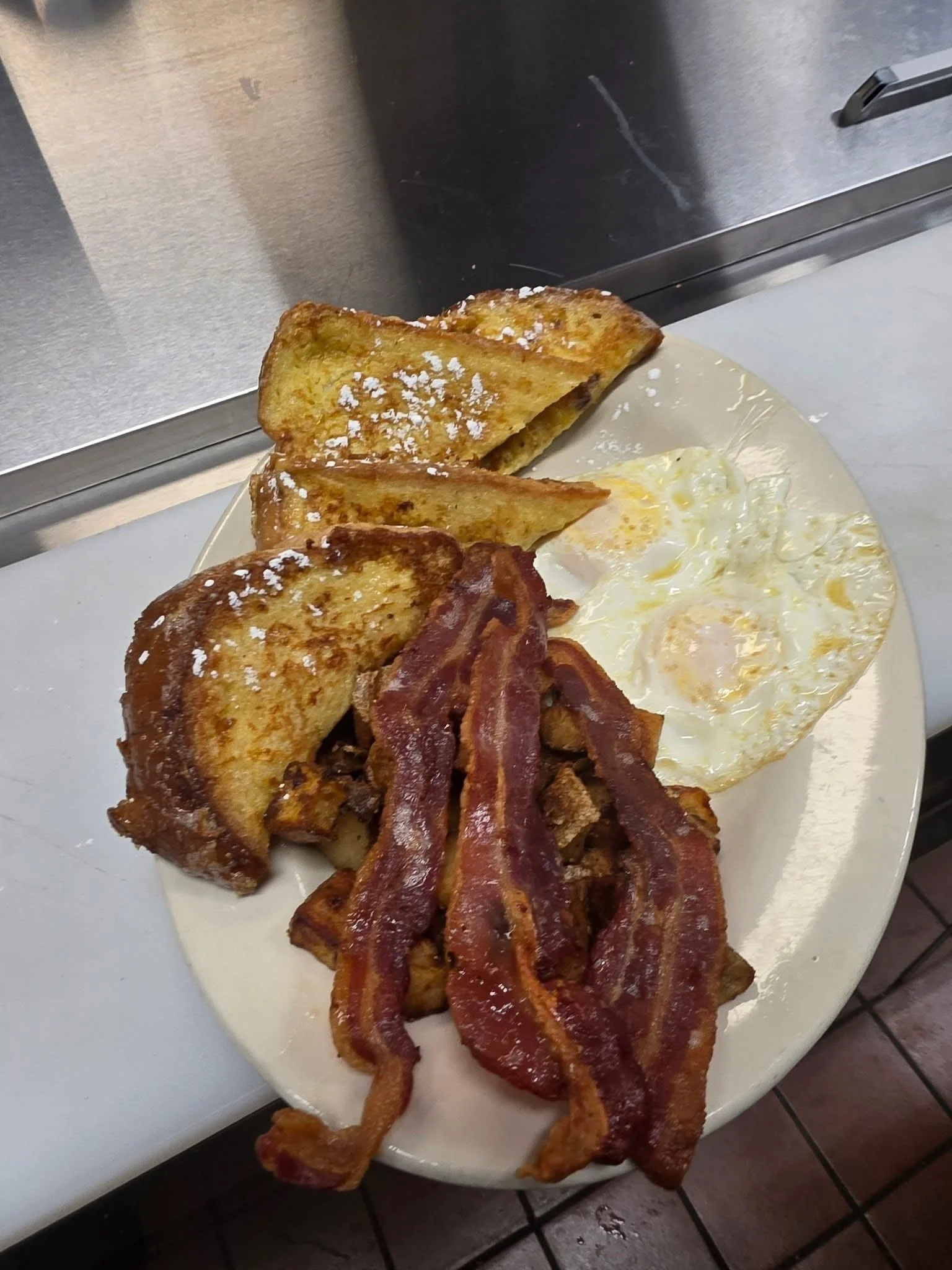 A breakfast plate with French toast, fried eggs, bacon, and hash browns.