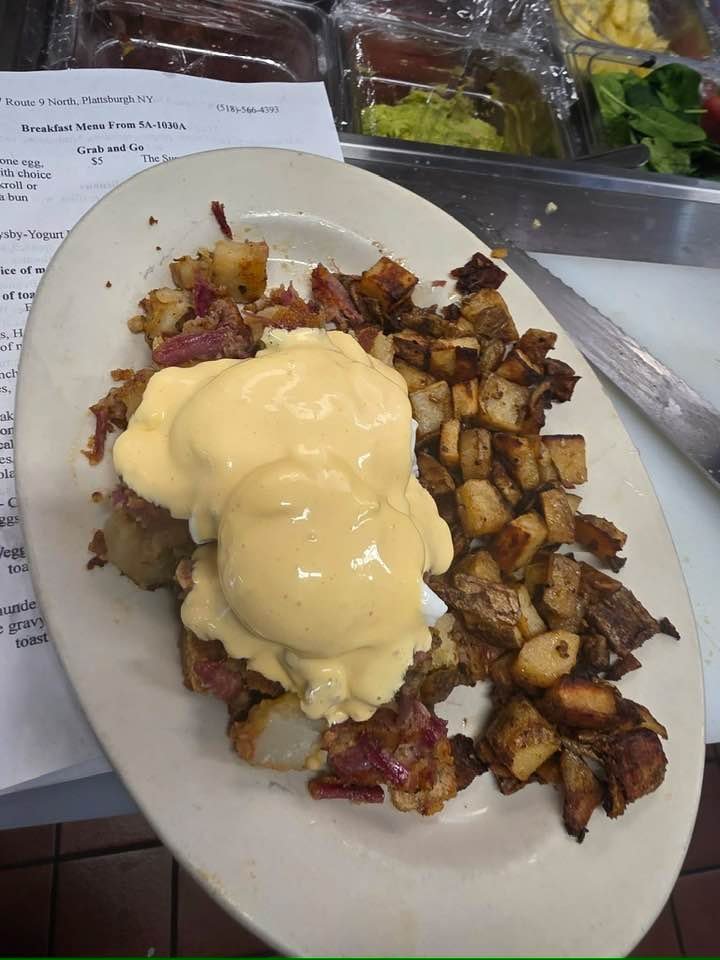 A plate of breakfast food with scrambled eggs topped with hollandaise sauce, crispy bacon, and crispy breakfast potatoes.