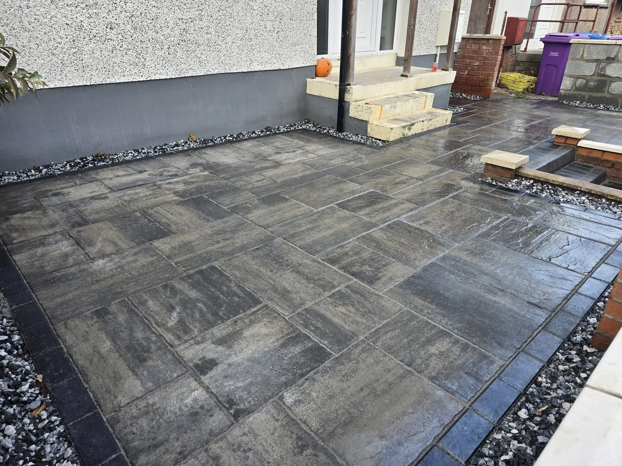 Recently finished dark gray stone patio in front of house, with steps leading up to the porch, surrounded by small decorative rocks along the edges.