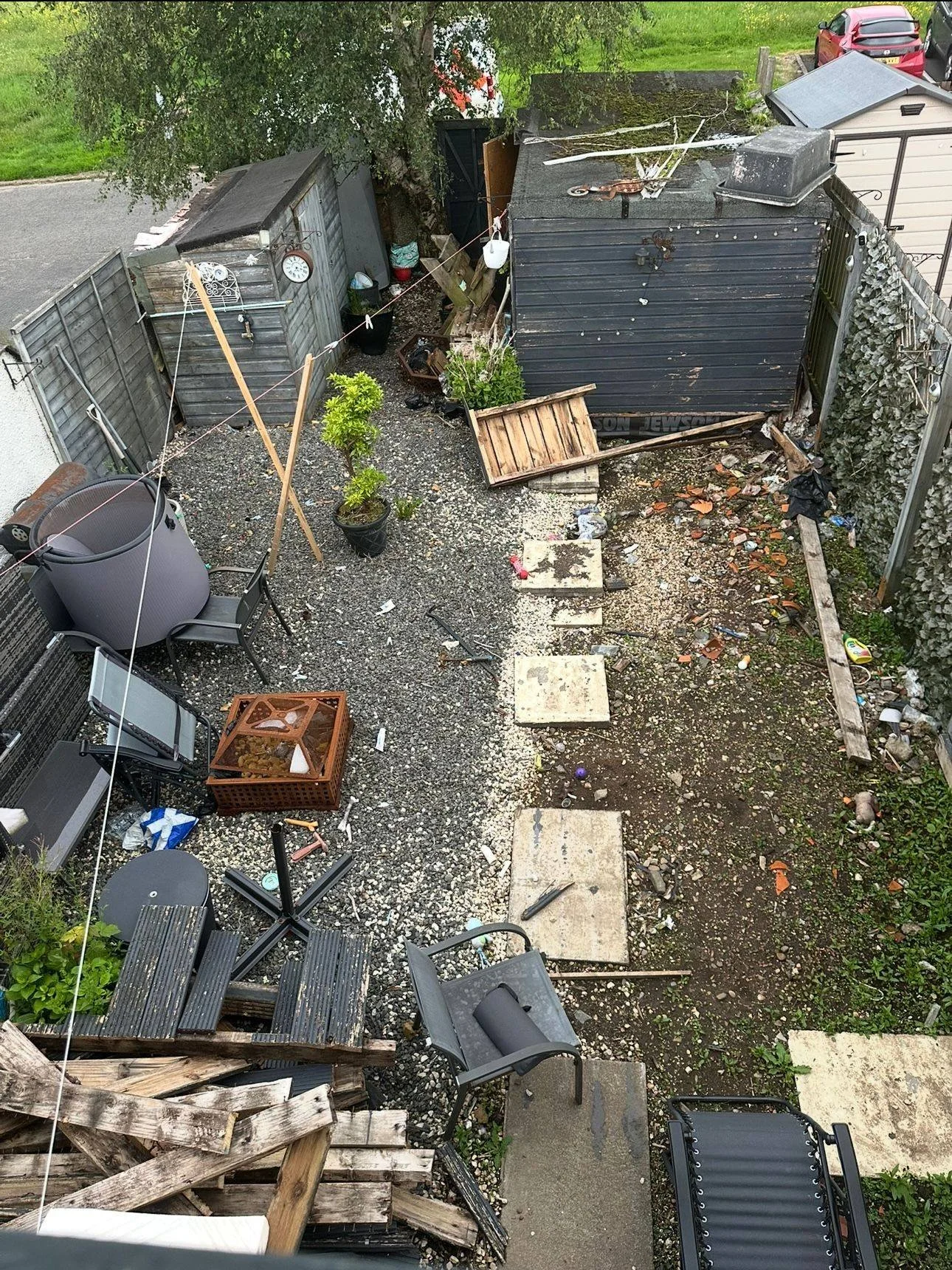 Backyard scene with damaged fence, scattered debris, broken furniture, and a small shed.