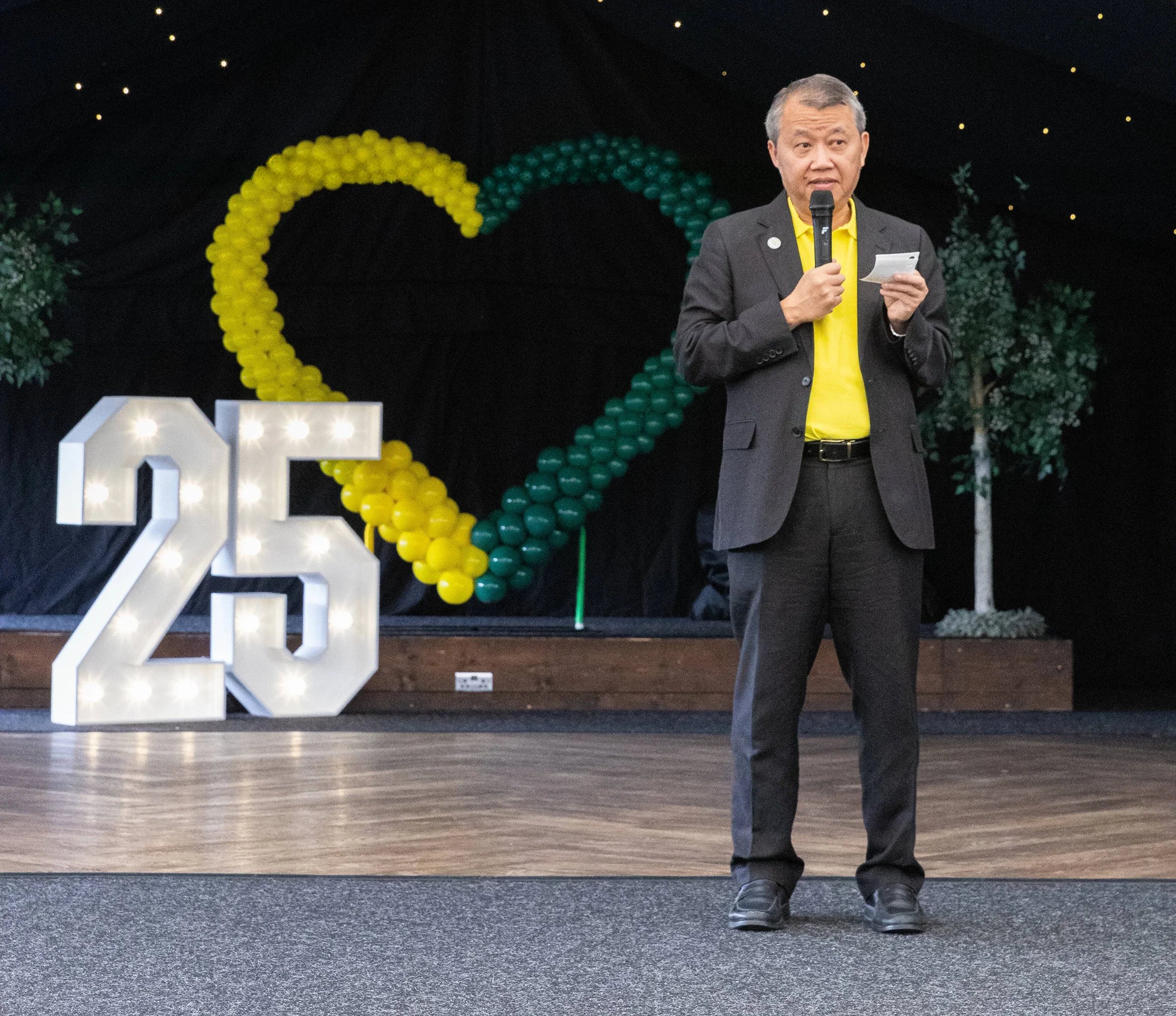Man speaking into microphone at charity event with balloon display shaped like heart behind him