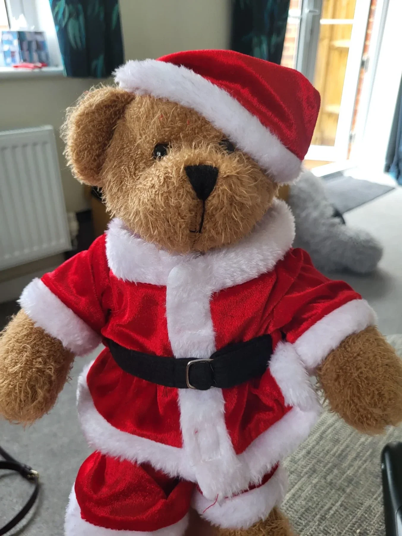 Teddy bear dressed in red Santa outfit with hat and belt sitting indoors