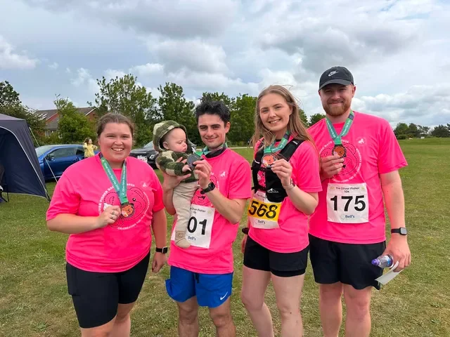 Team Oakley wearing pink race shirts holding their medals smiling with baby Oakley