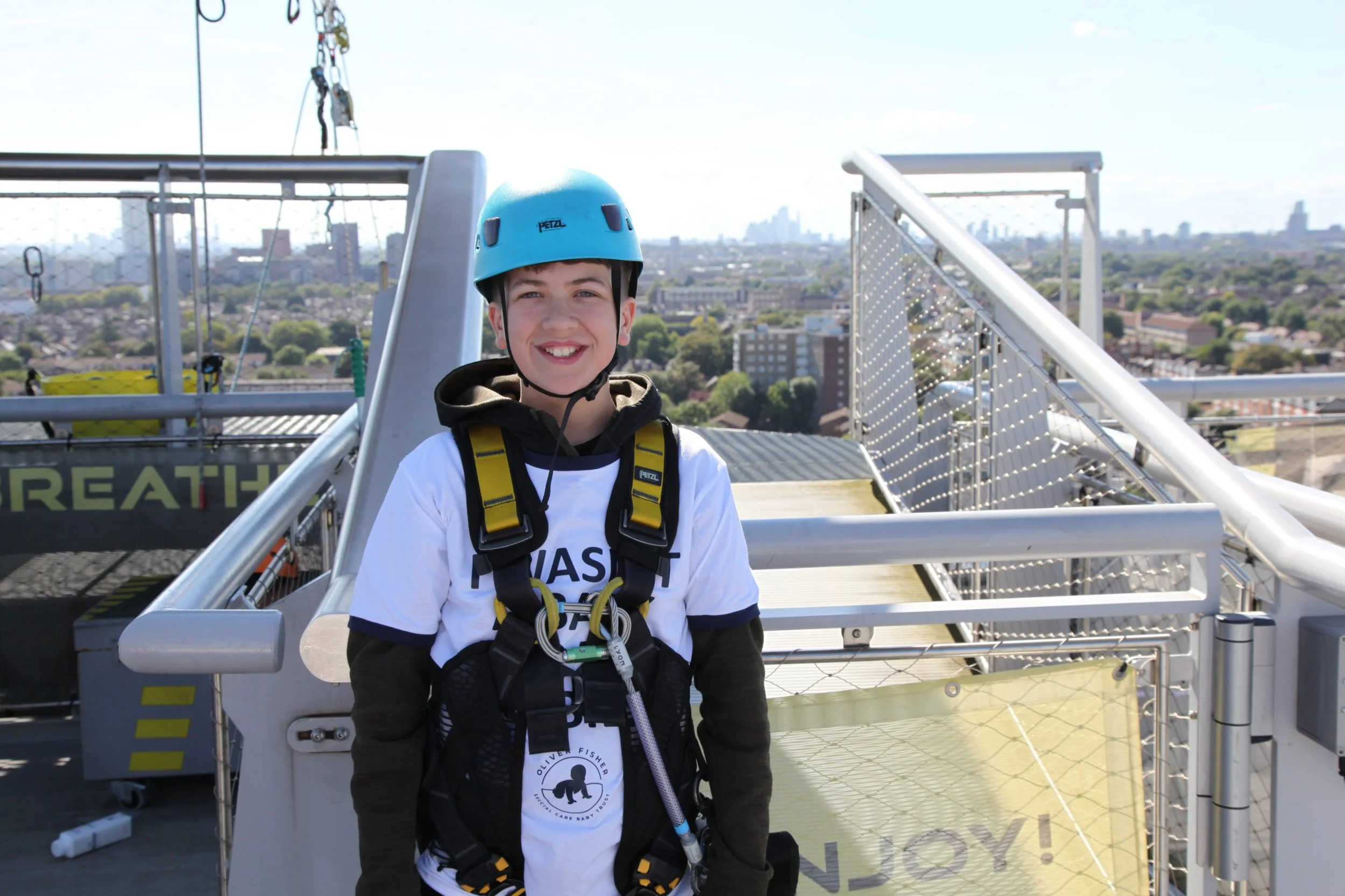 Young person wearing helmet and safety harness smiling on rooftop platform before challenge
