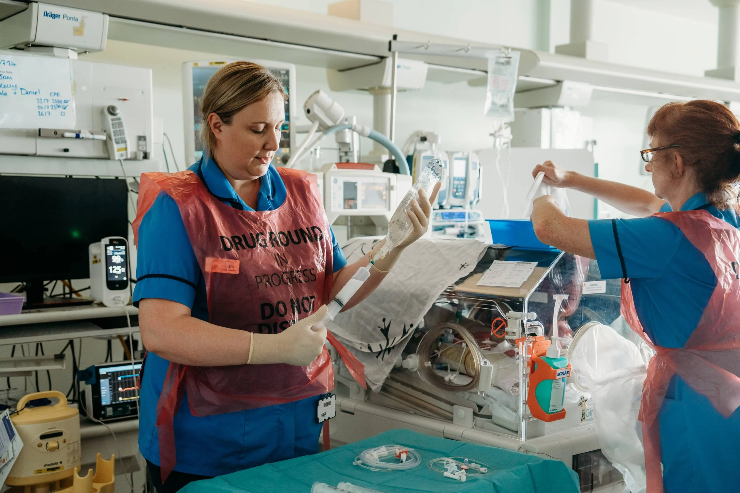 Premature baby lying in incubator with patterned blanket while a nurse provides care in hospital setting