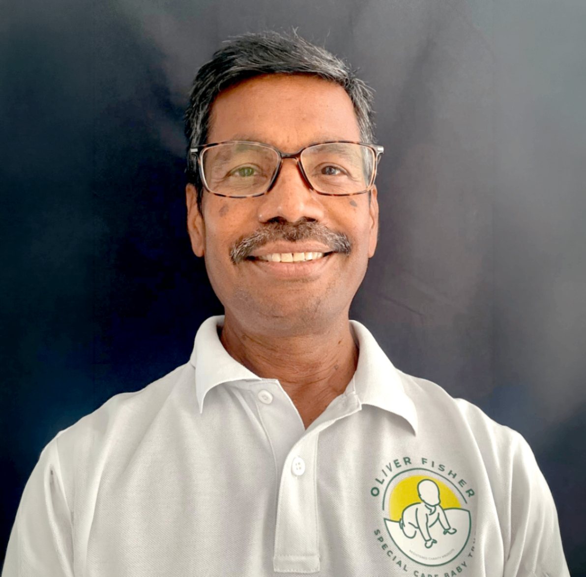 Man smiling wearing black glasses white polo shirt with charity logo on plain background