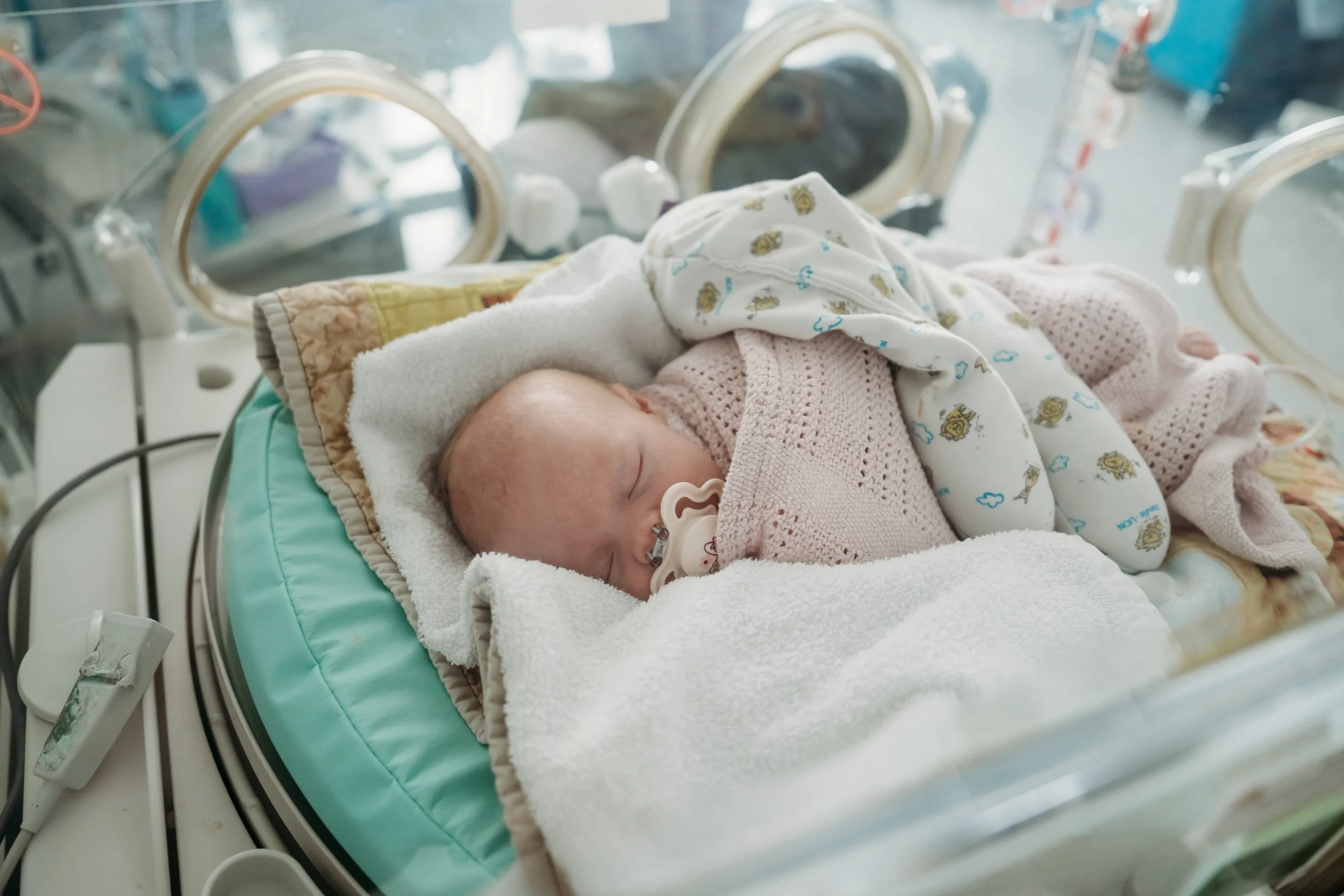 Sleeping newborn baby wrapped in blankets inside neonatal incubator in hospital unit