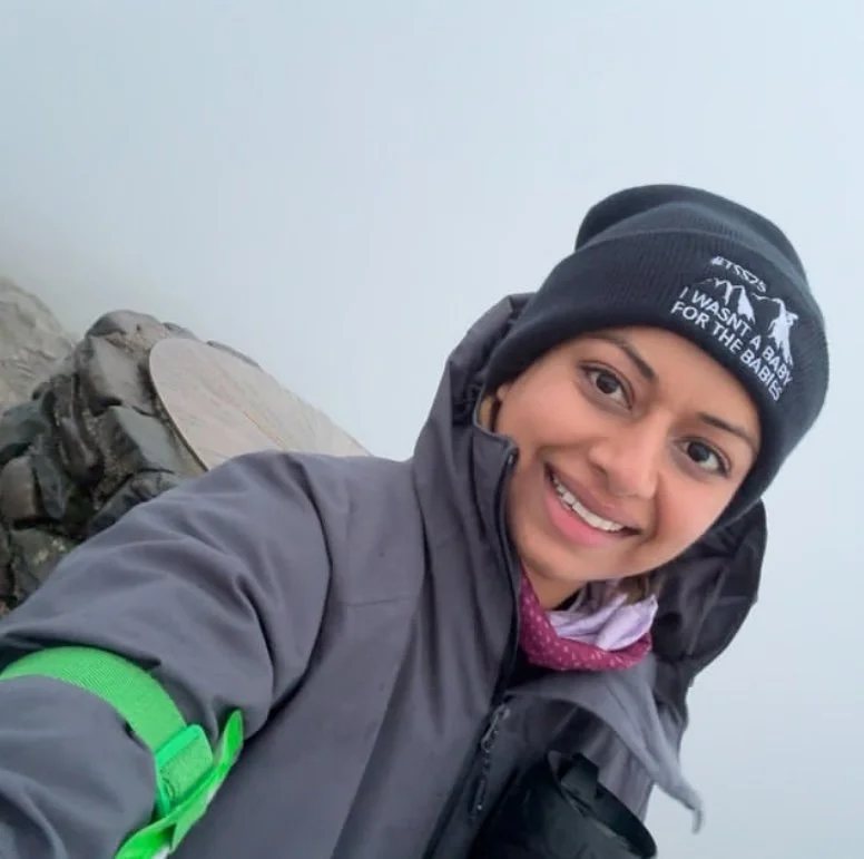 Woman taking selfie while hiking on mountain wearing outdoor clothing and hat in misty rocky landscape