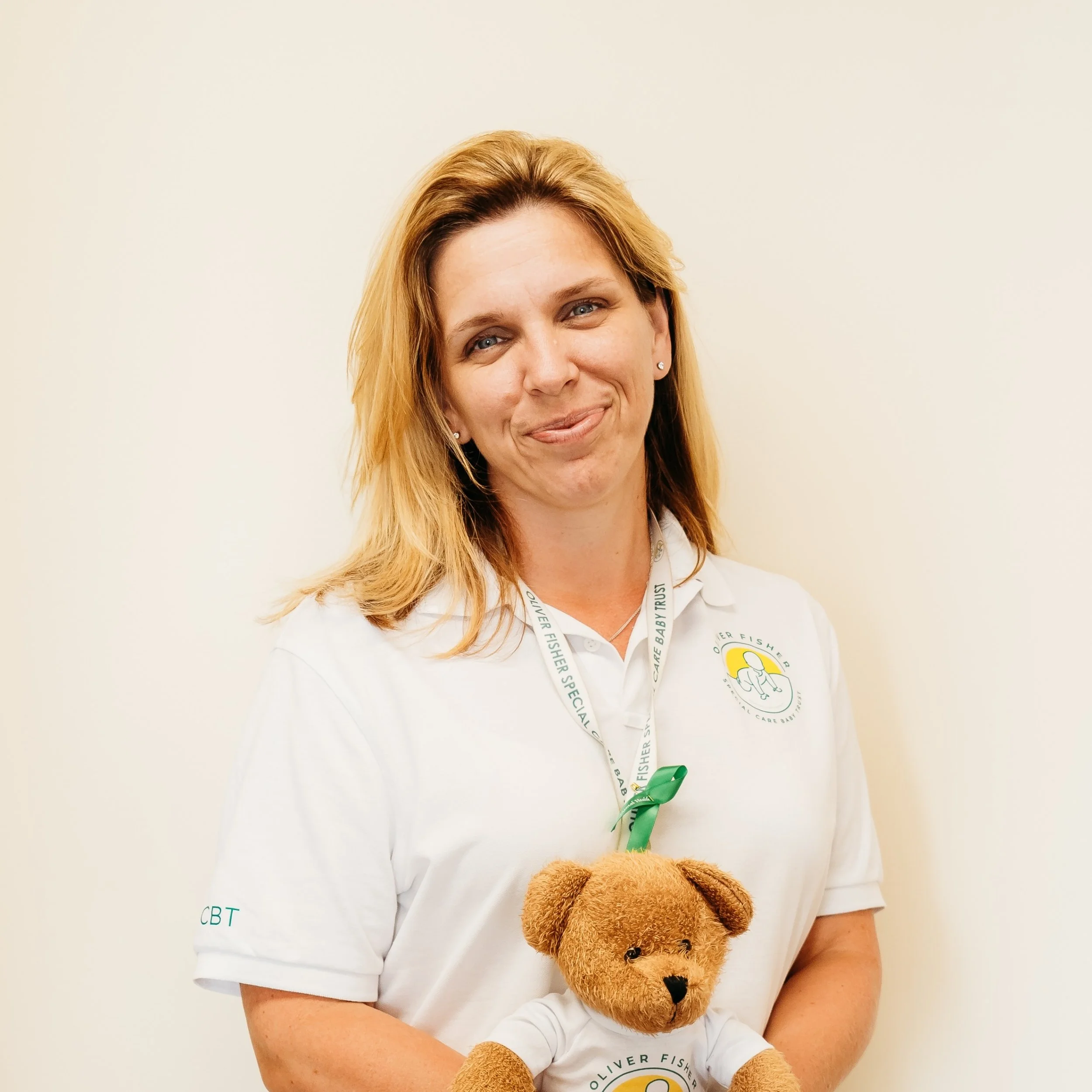Woman wearing white Oliver Fisher polo shirt holding teddy bear smiling in portrait-style image