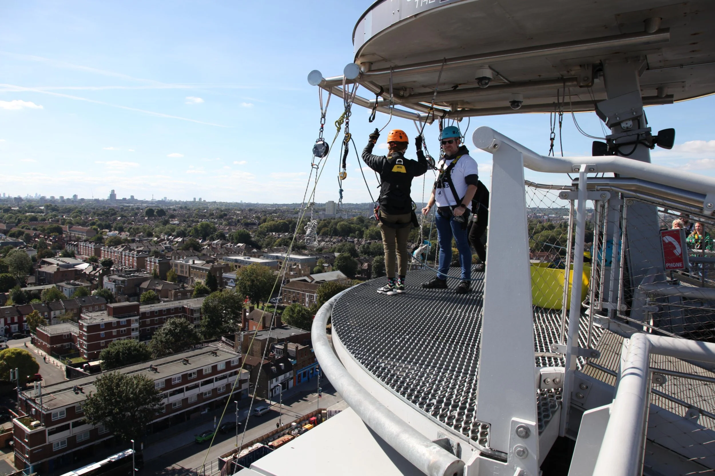 Two participants clipped into safety harnesses preparing to abseil from high platform overlooking city