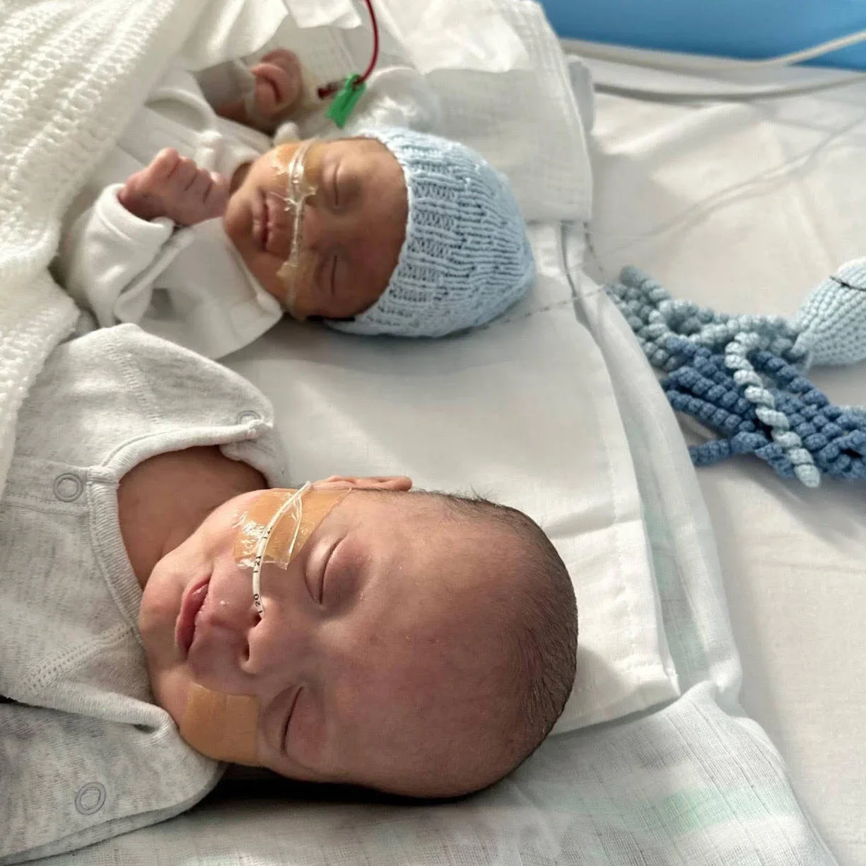 Photo of Oliver and Louie, in the special care baby unit, asleep, with feeding tubes, all snuggled up under blankets