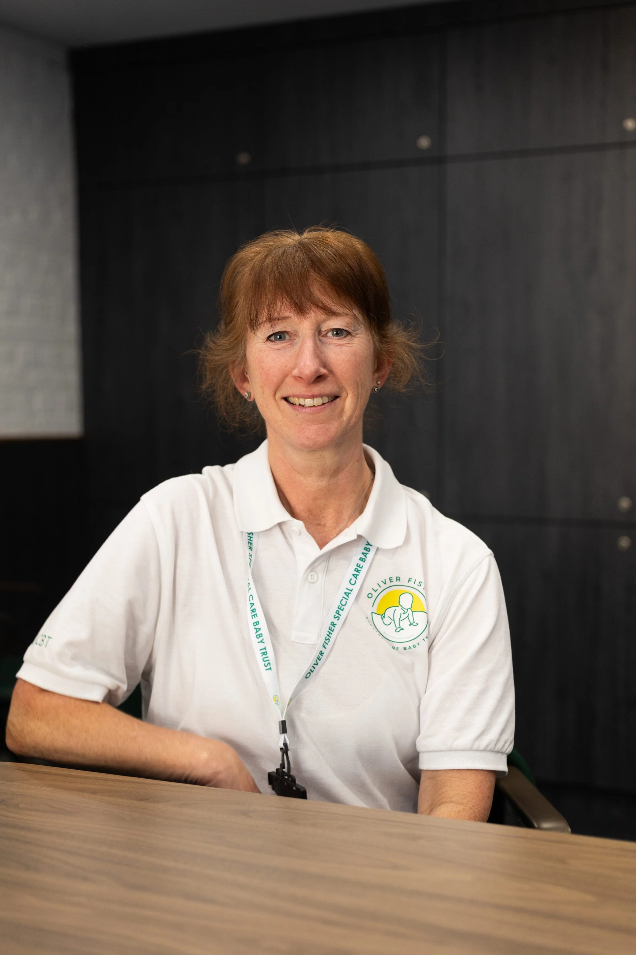 Woman smiling wearing white polo shirt with charity logo on plain background