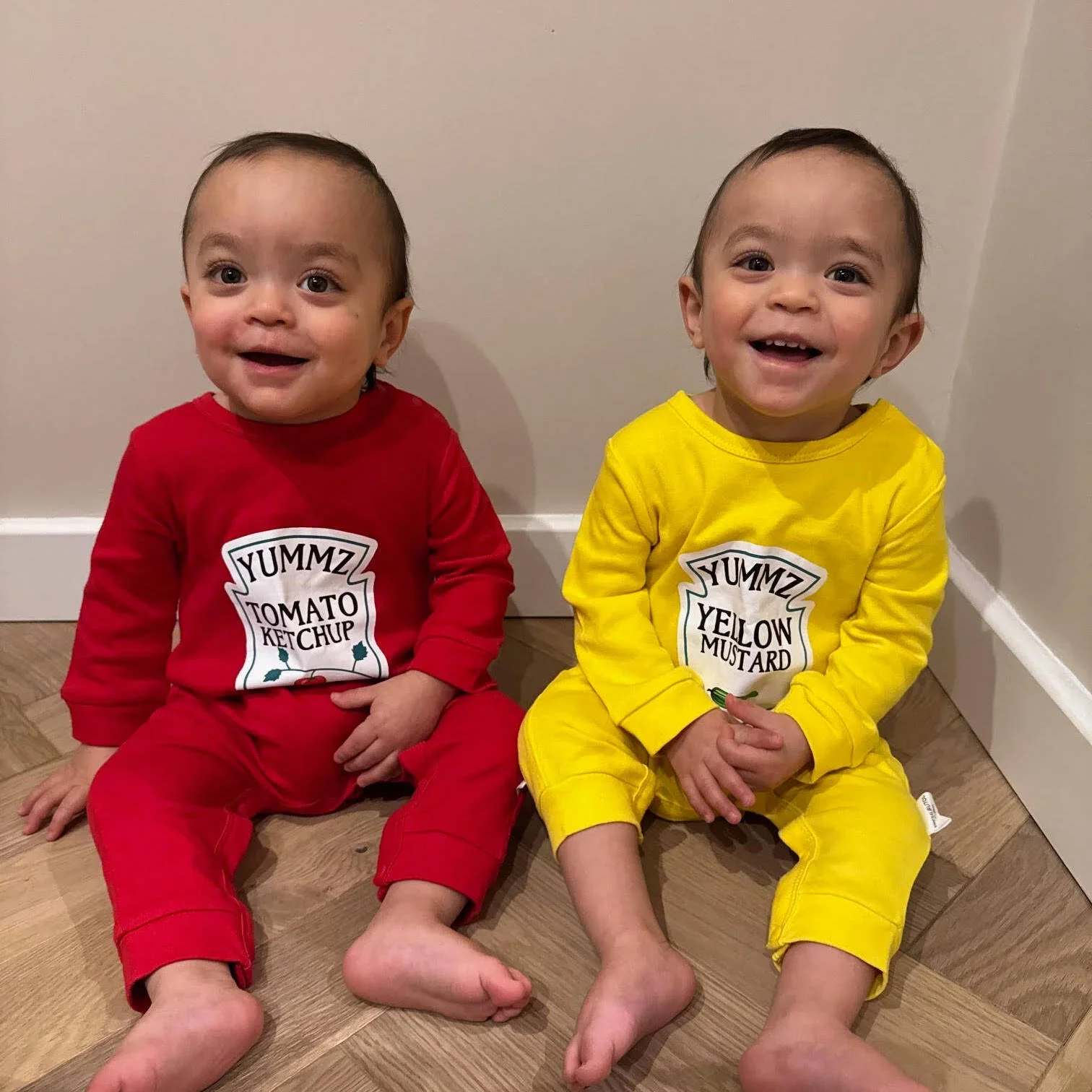 Photo of Oliver & Louie now, one in a heinz tomato ketchup onesie, another in a heinz mustard onesie, both with a huge grin on their faces
