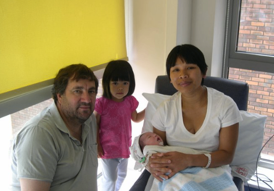 Family in the corner of a NICU room holding a baby connected with tubes and wires