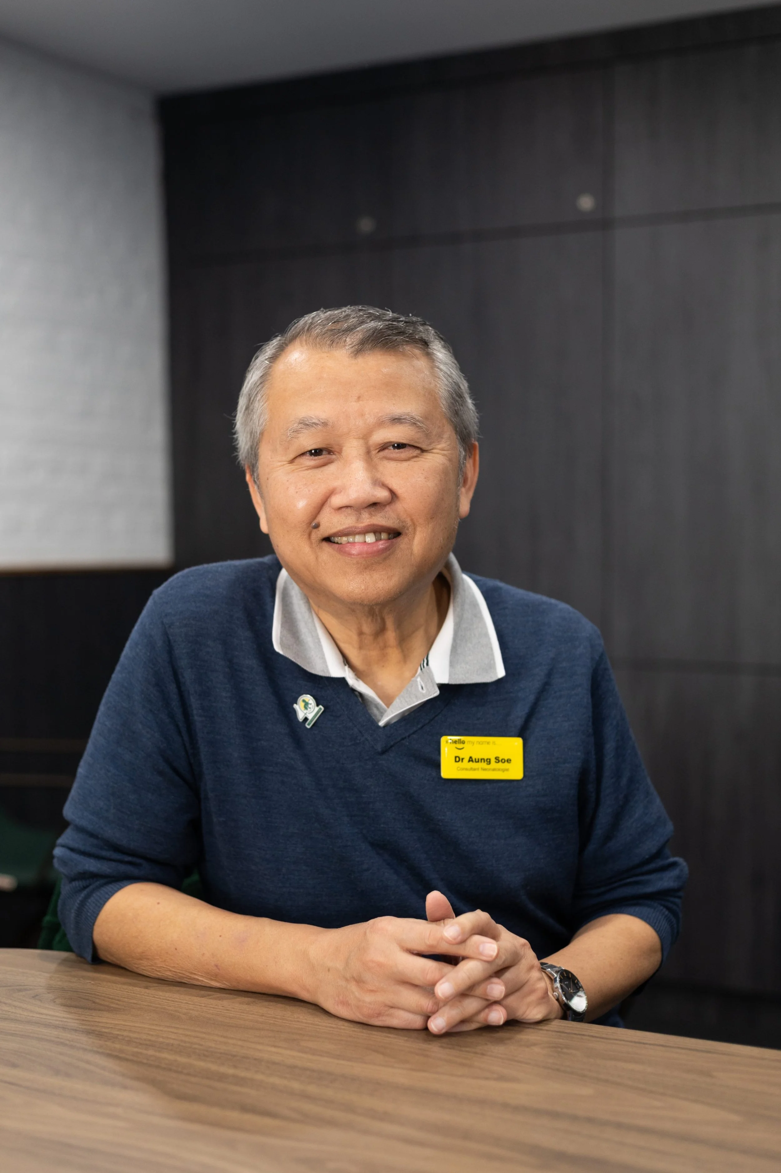 Man wearing blue polo shirt smiling with plain background