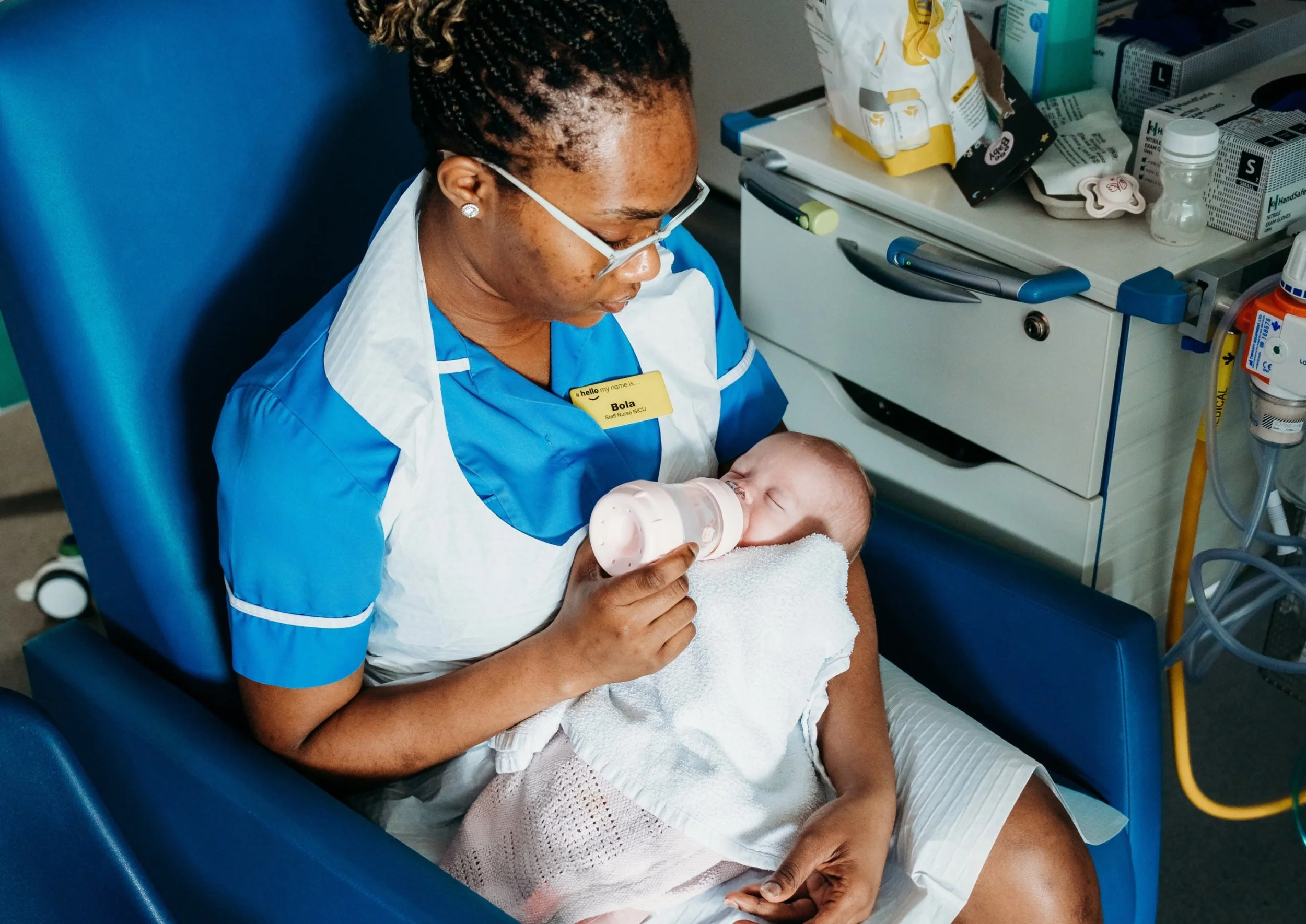 Nurse bottle feeding newborn baby wrapped in blanket on the neonatal unit