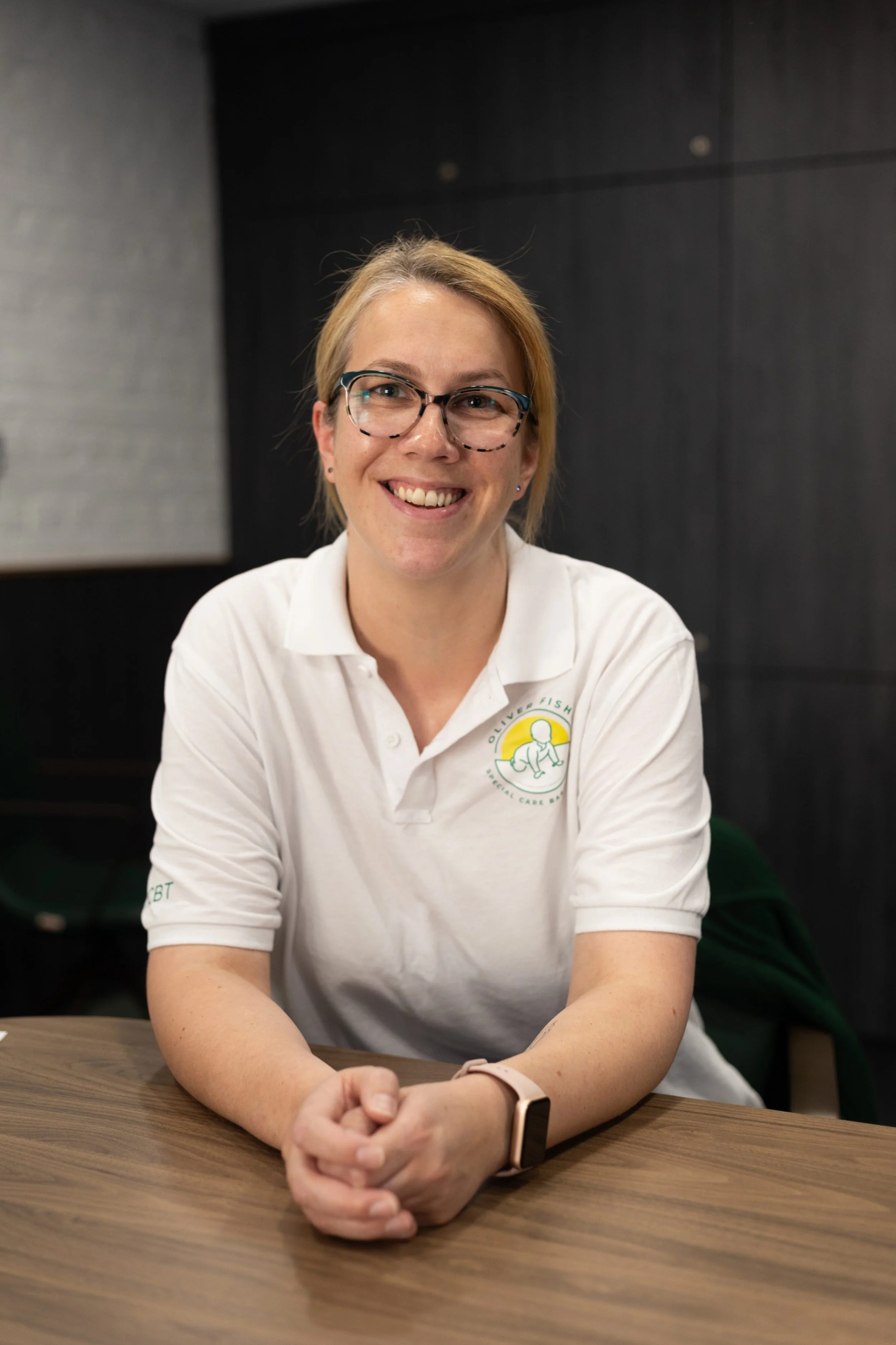 Woman smiling wearing white polo shirt with charity logo on plain background