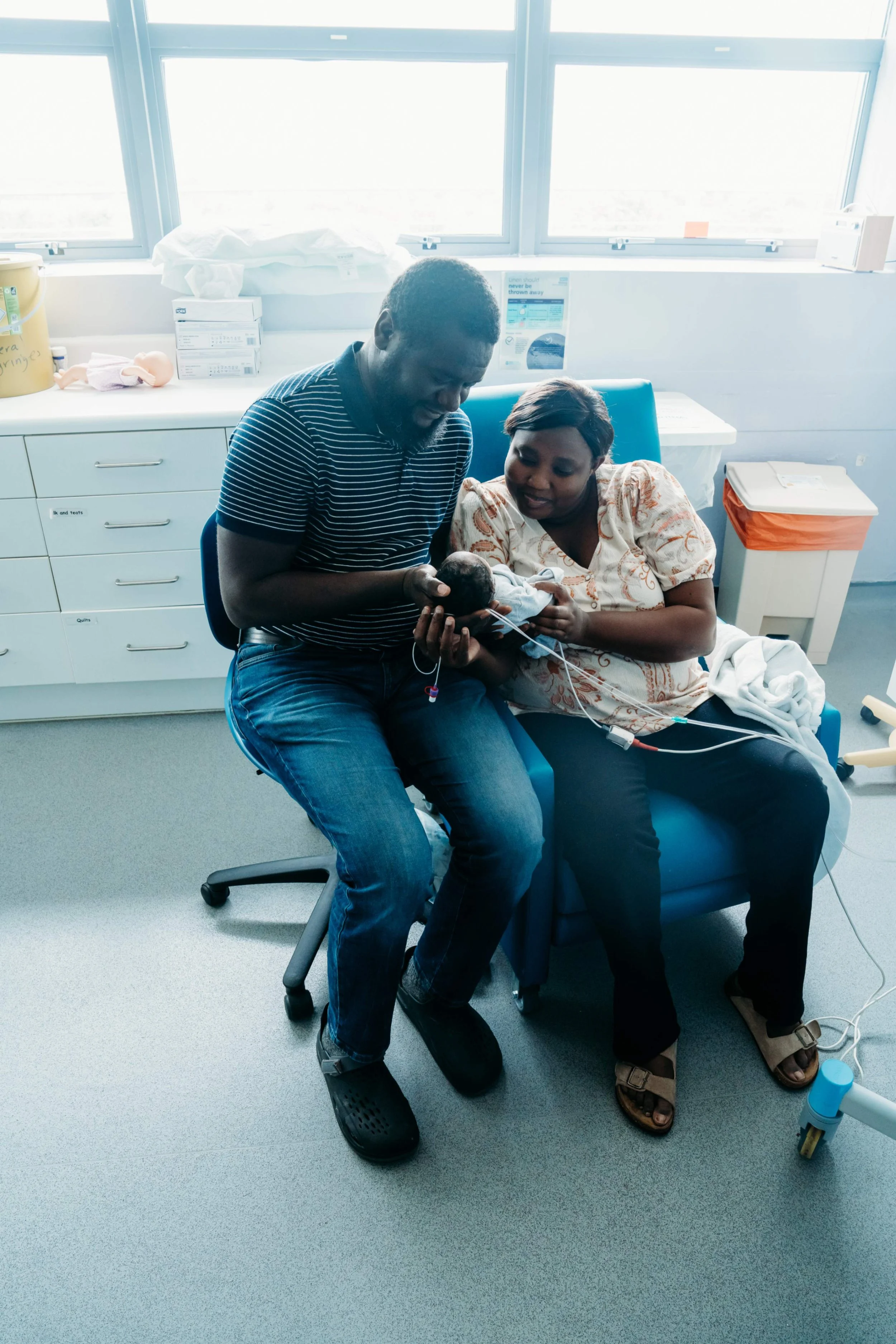 Two parents sitting together in hospital room gently holding their newborn baby and looking down at them with care
