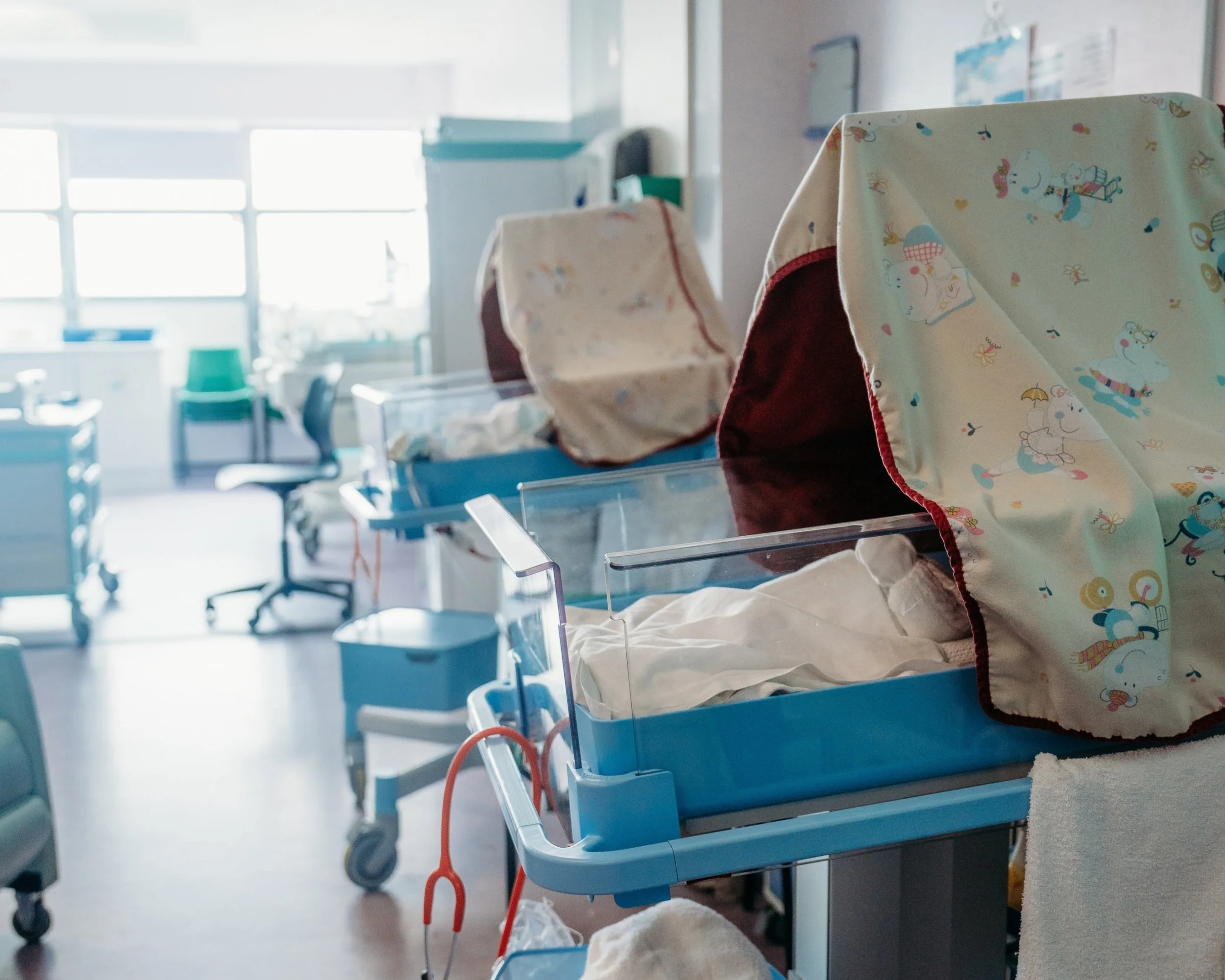 Newborn baby lying in hospital cot surrounded by blankets and medical support equipment in a neonatal unit