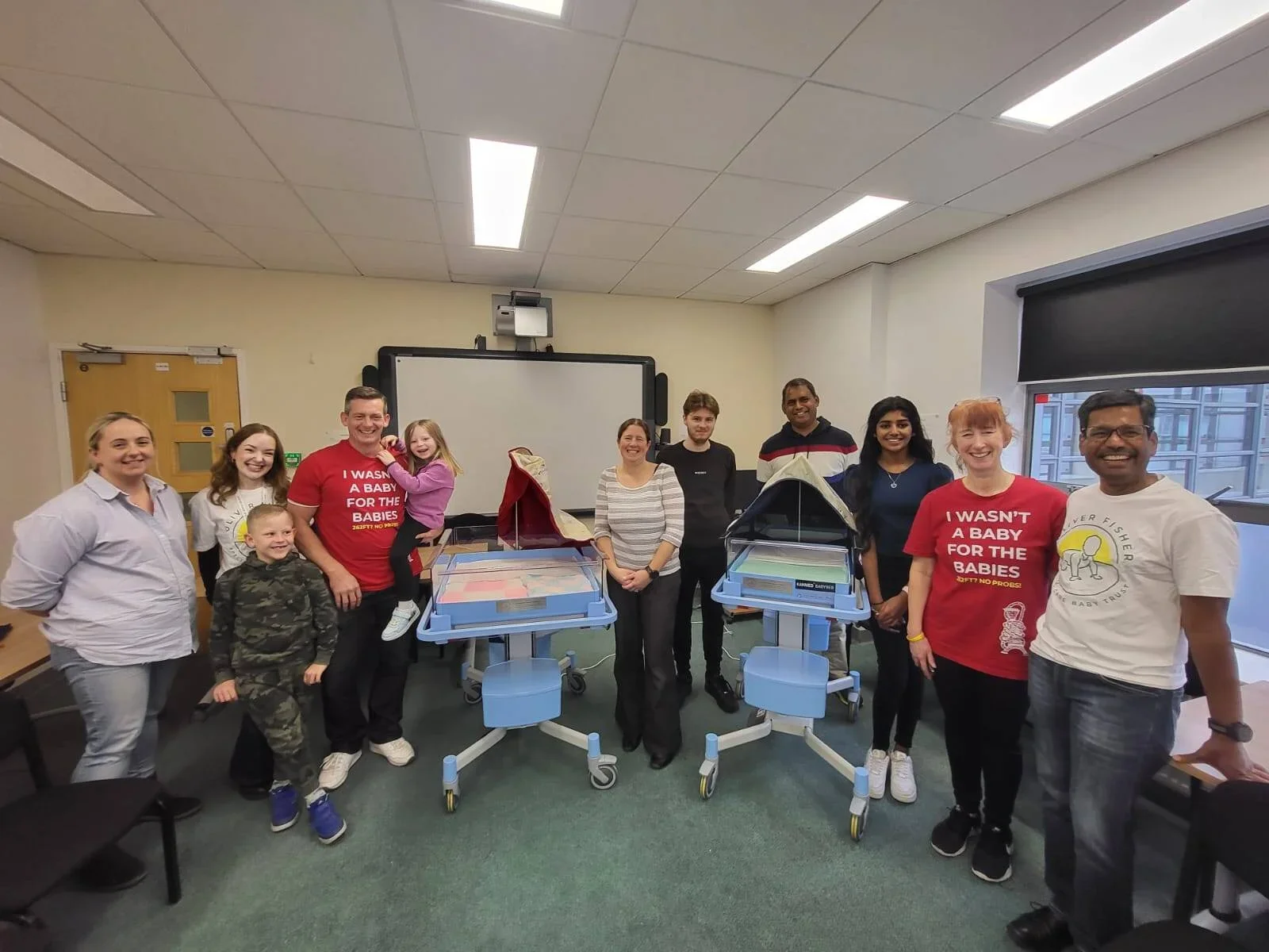 Group of staff and supporters standing with neonatal equipment at hospital event